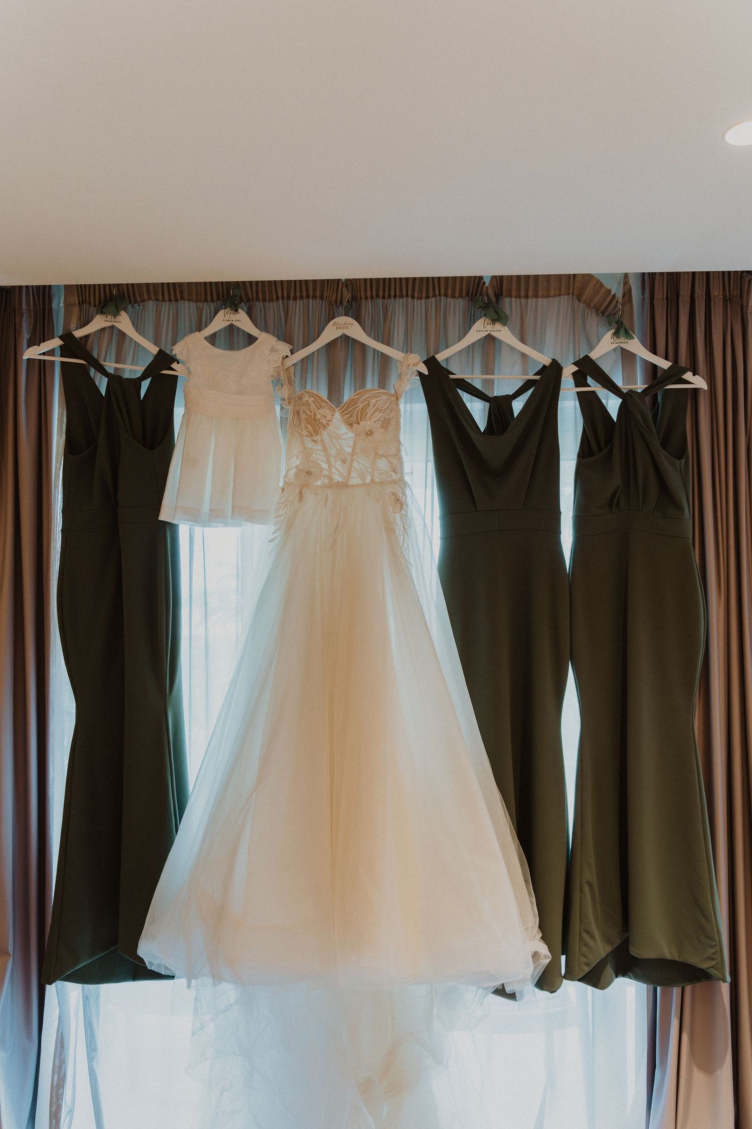 Wedding dresses and bridesmaid gowns hanging on display against brown curtains.