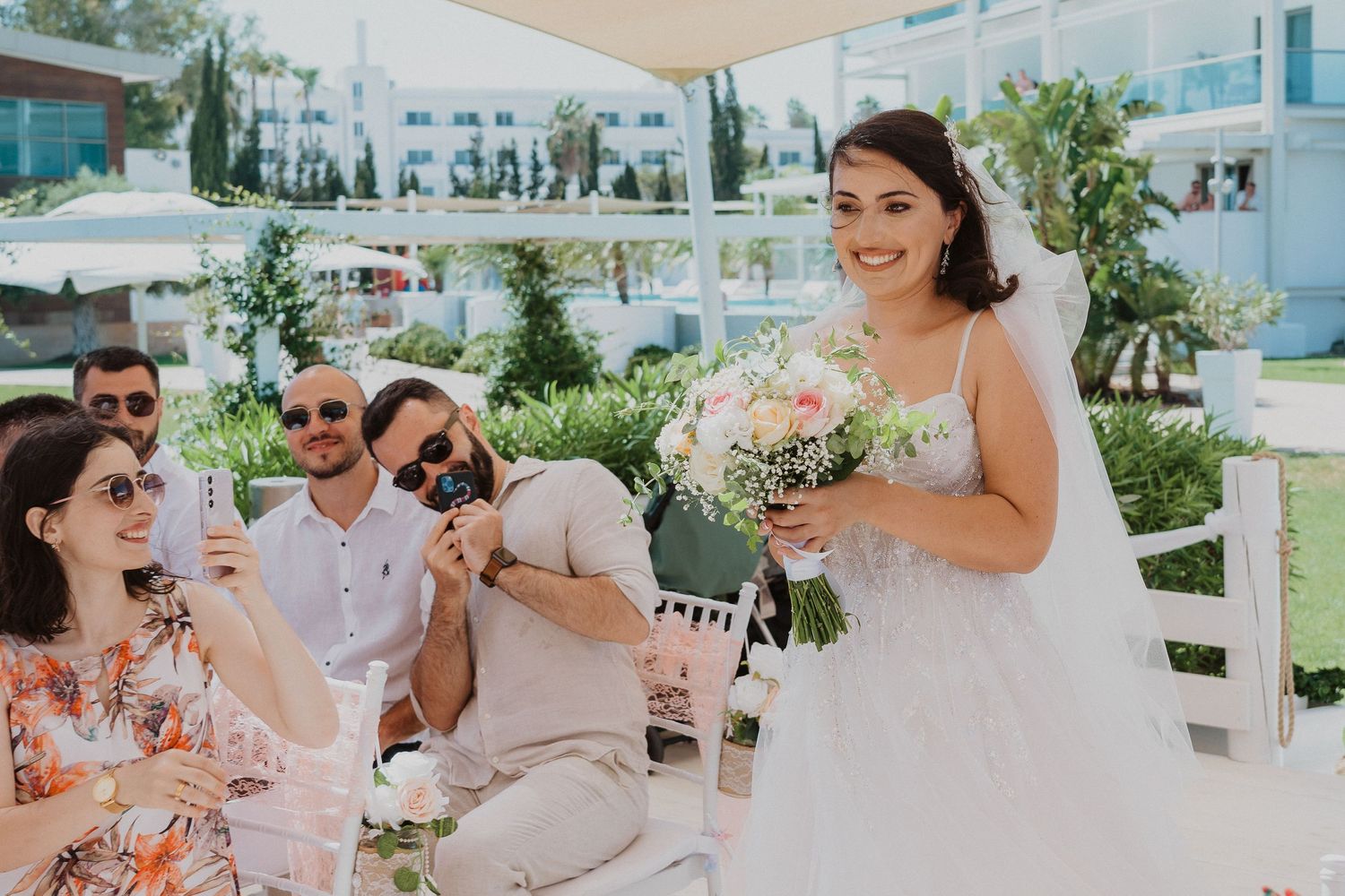 Wedding celebration on an outdoor terrace with laughter and joy as someone holds a bouquet of pink flowers.
