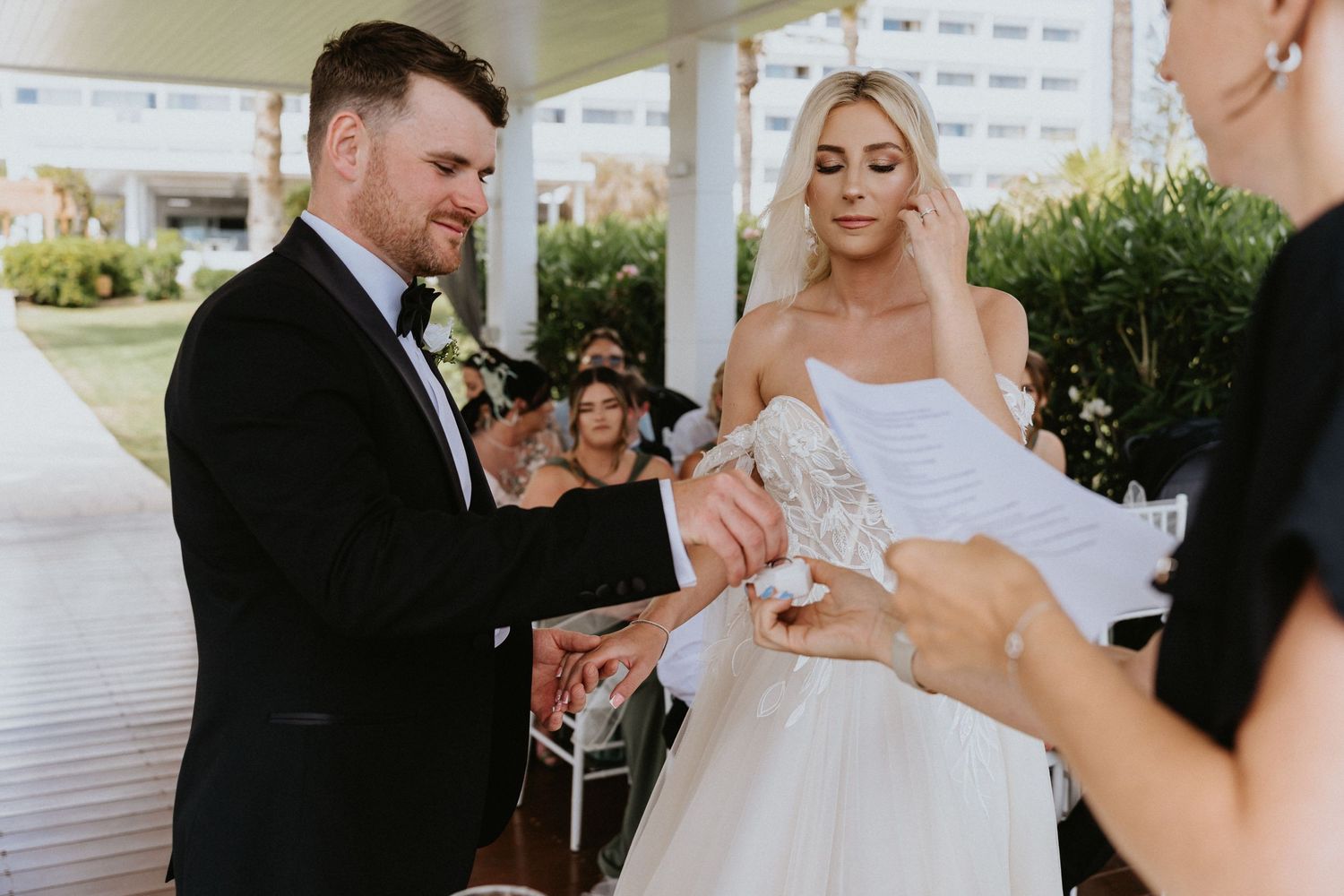 Exchange of rings during waterfront wedding ceremony under covered pavilion.