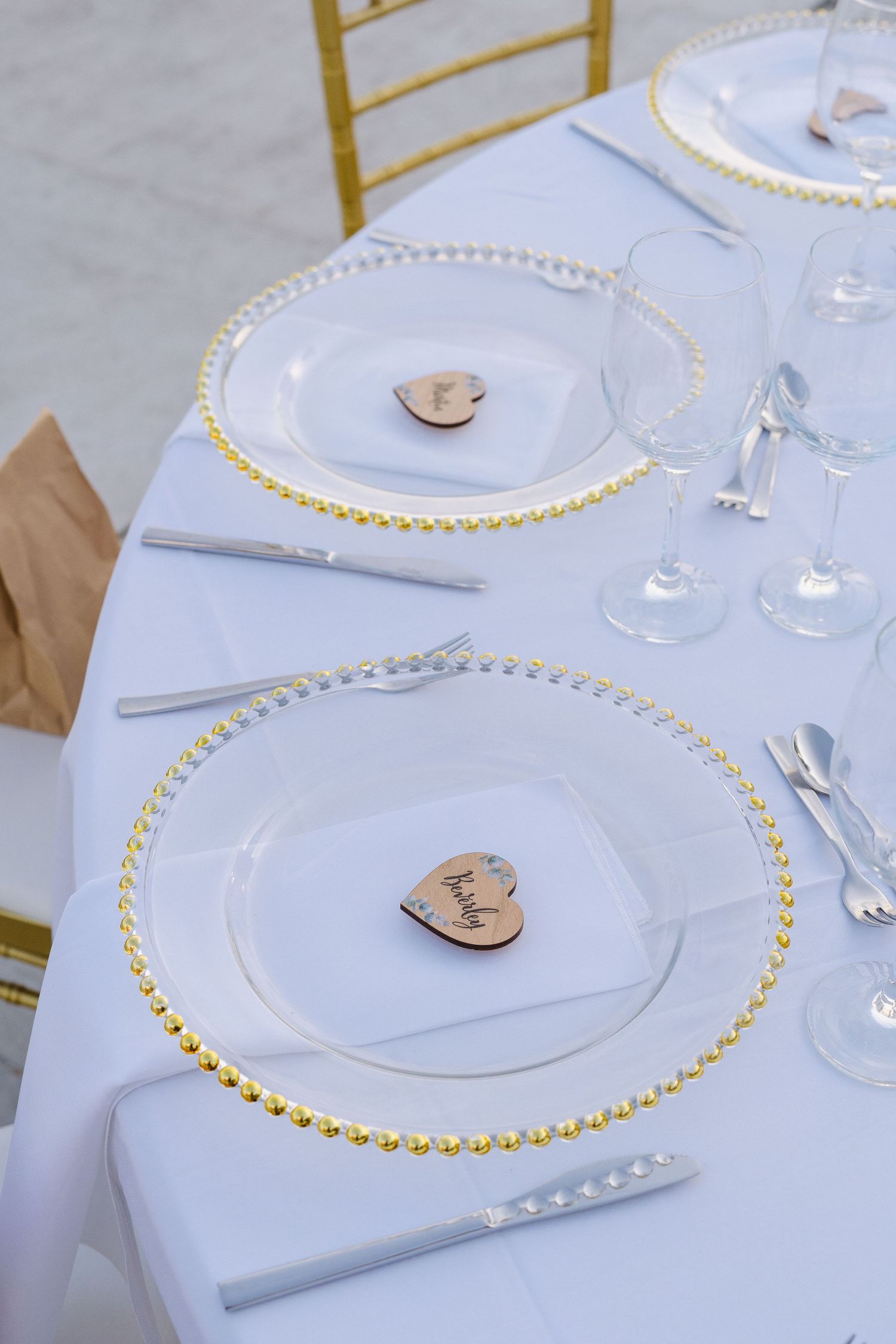 Wedding table setting with gold-rimmed glass charger plates and wooden heart decorations.