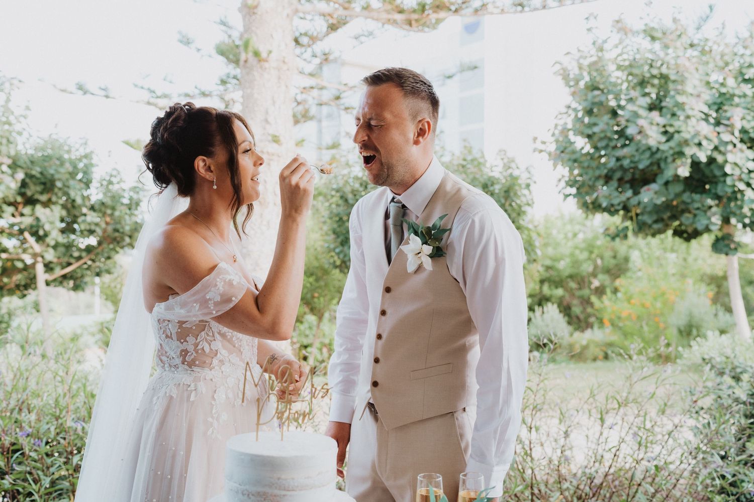 A couple shares a heartfelt moment outdoors during their wedding ceremony amidst a sunlit garden setting.