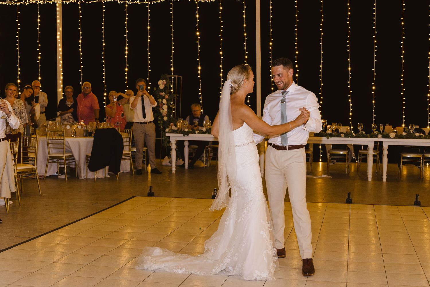 A couple shares an intimate moment during their first dance at a beautifully lit reception venue.