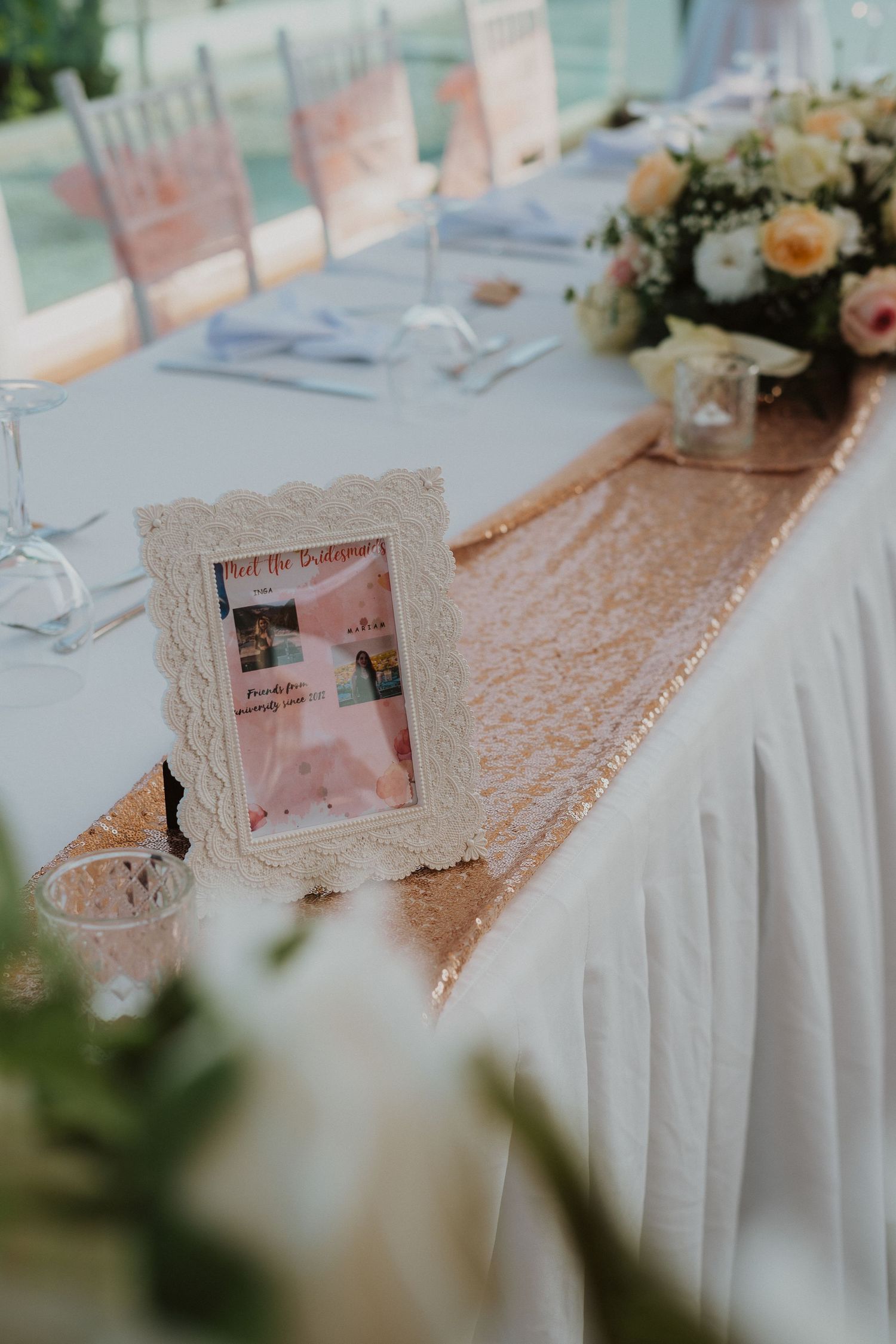 Wedding reception table with rose gold sequin runner and vintage white photo frame on crisp white linens.