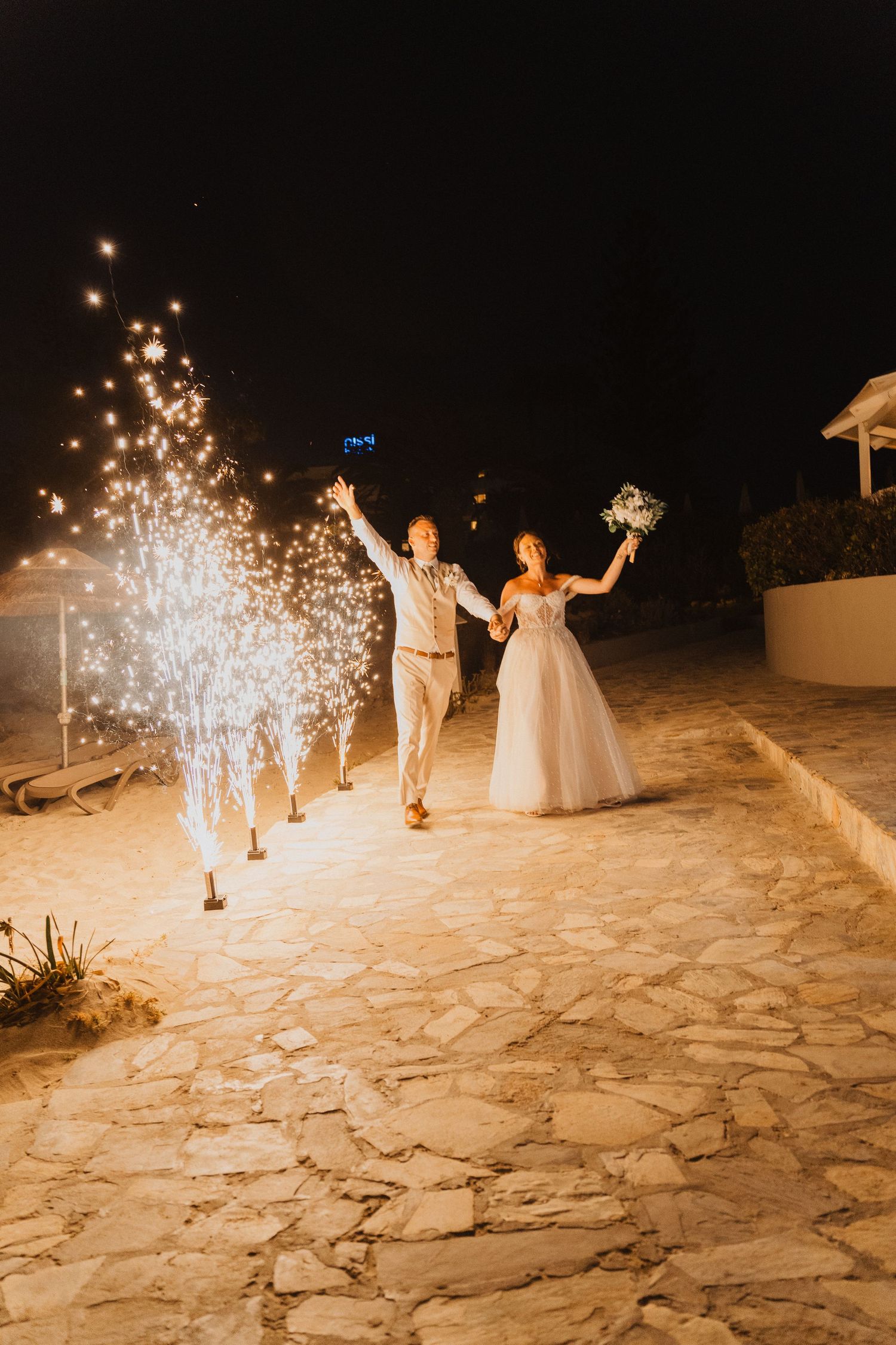A joyful couple celebrating at night on a stone path with glowing sparkler fountains creating a magical atmosphere.