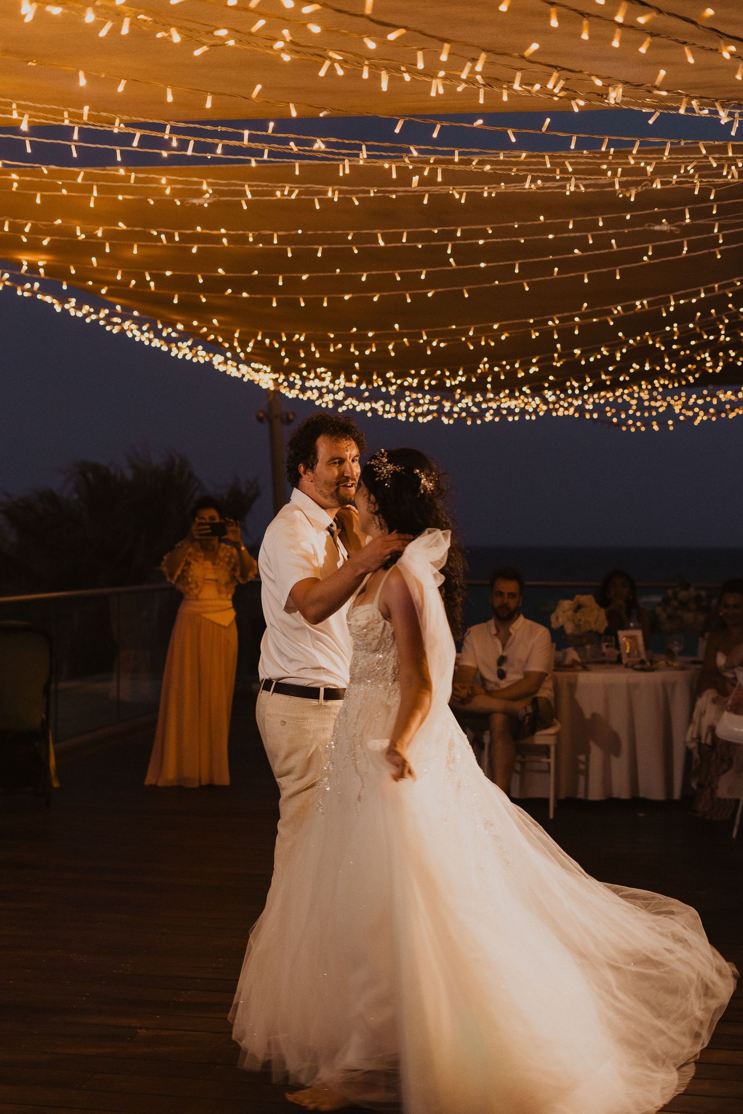 A romantic dance under warm string lights at an outdoor wedding reception at dusk.
