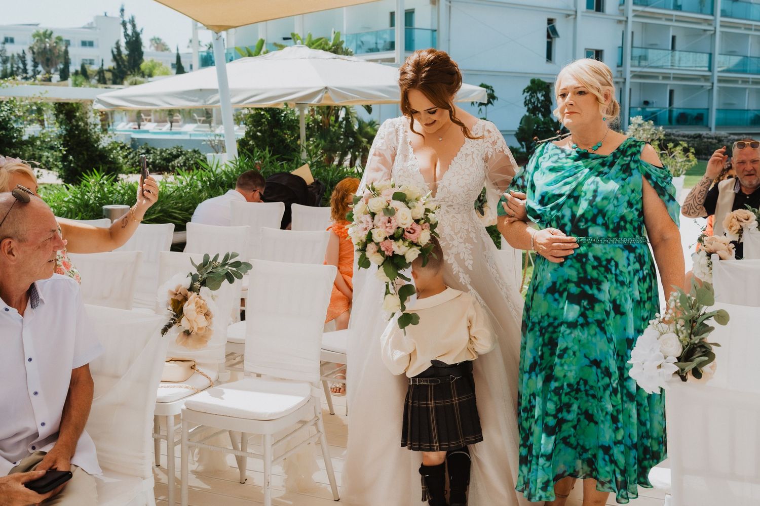 Wedding party members walking through outdoor venue with modern building in background.