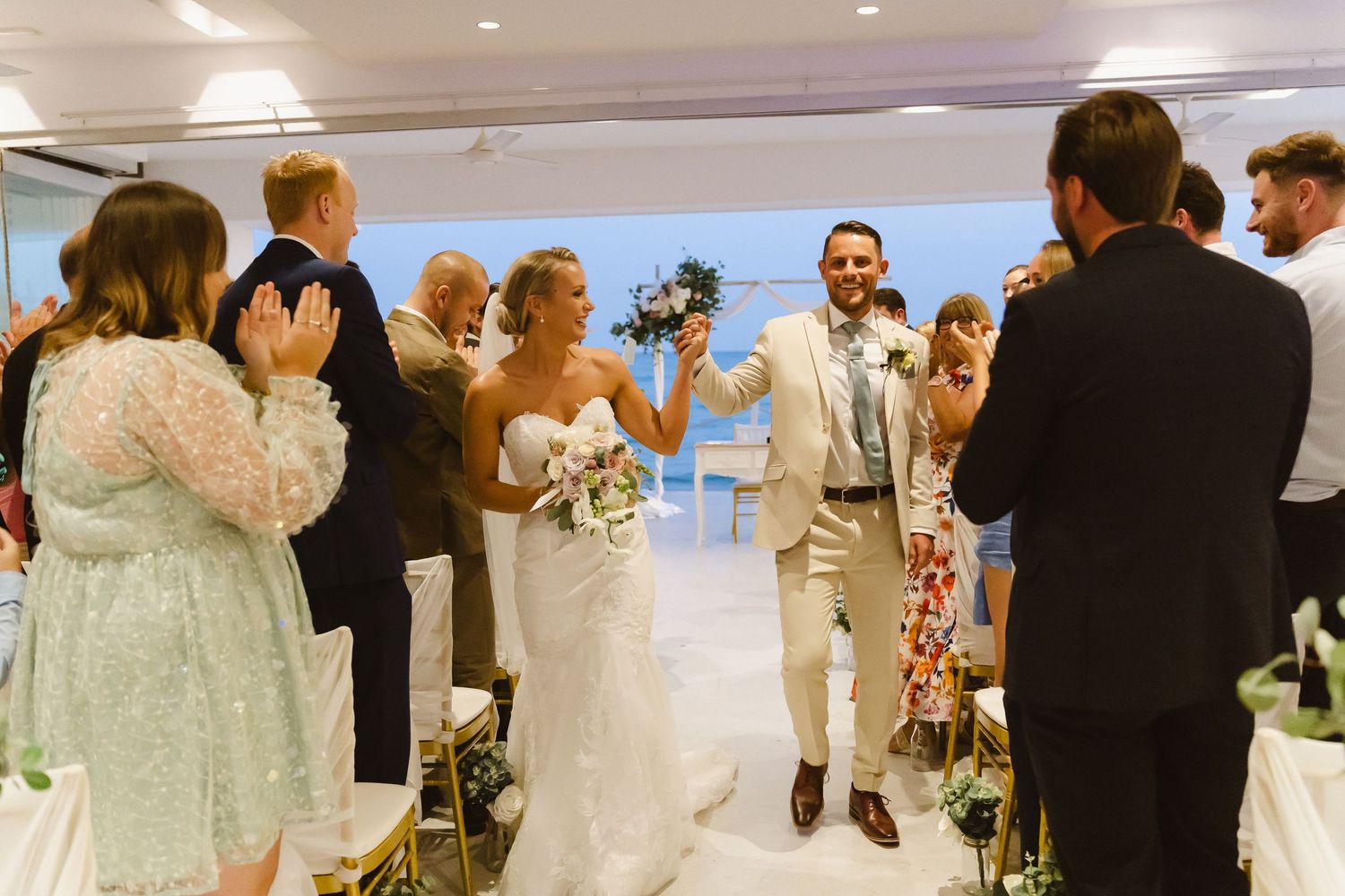 Celebratory recessional through indoor venue with flower-lined aisle and cheering guests.
