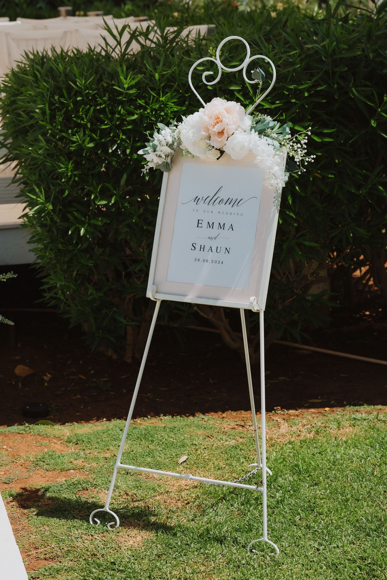 Elegant wedding welcome sign with floral decorations on a white metal easel stand.