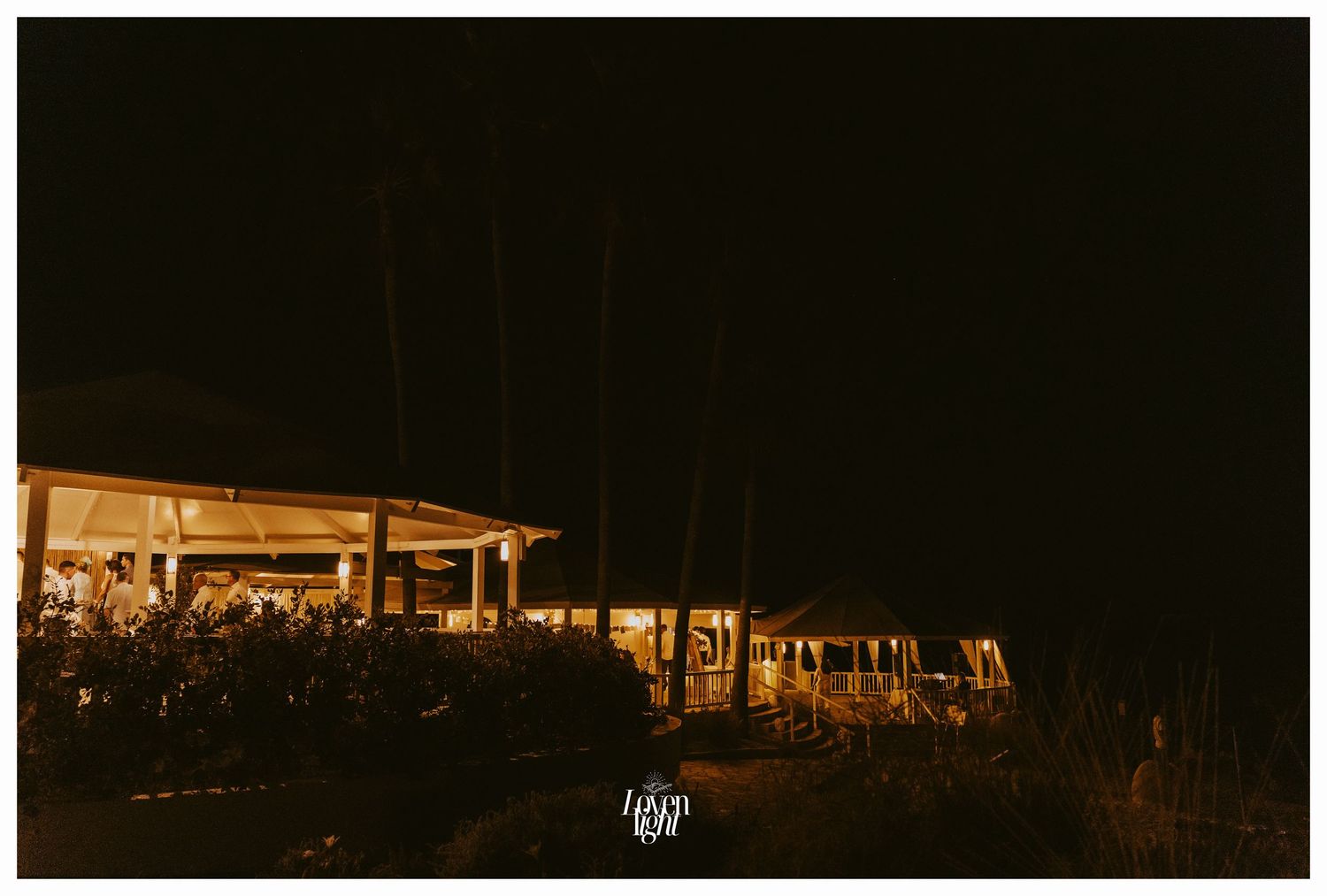 Illuminated outdoor venue at night with string lights and palm trees.