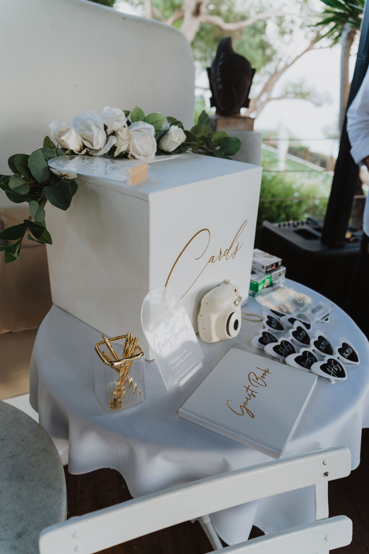 White wedding card box decorated with eucalyptus and gold lettering on a table with accessories.