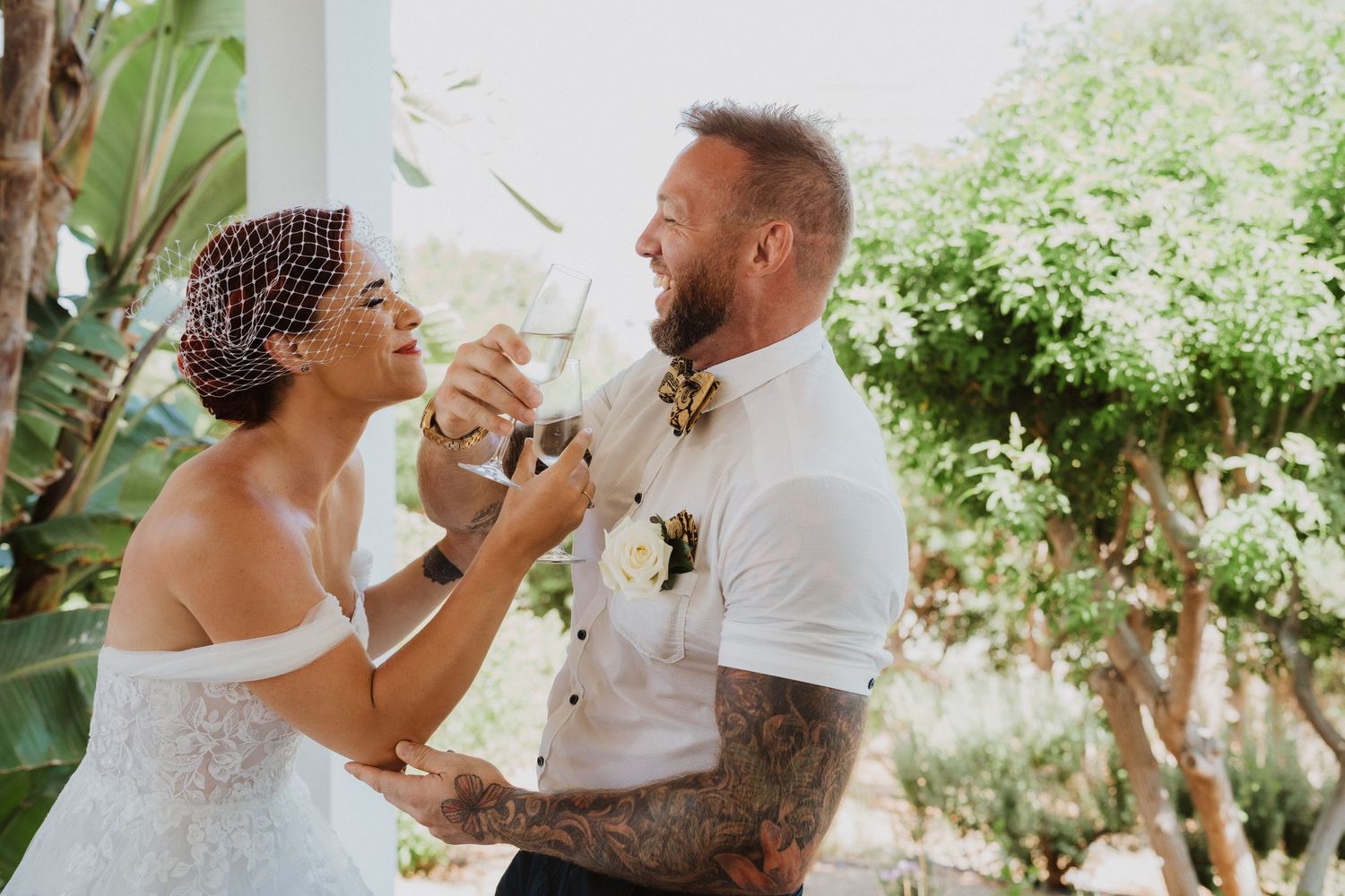Newlyweds playfully feed each other wedding cake outdoors.