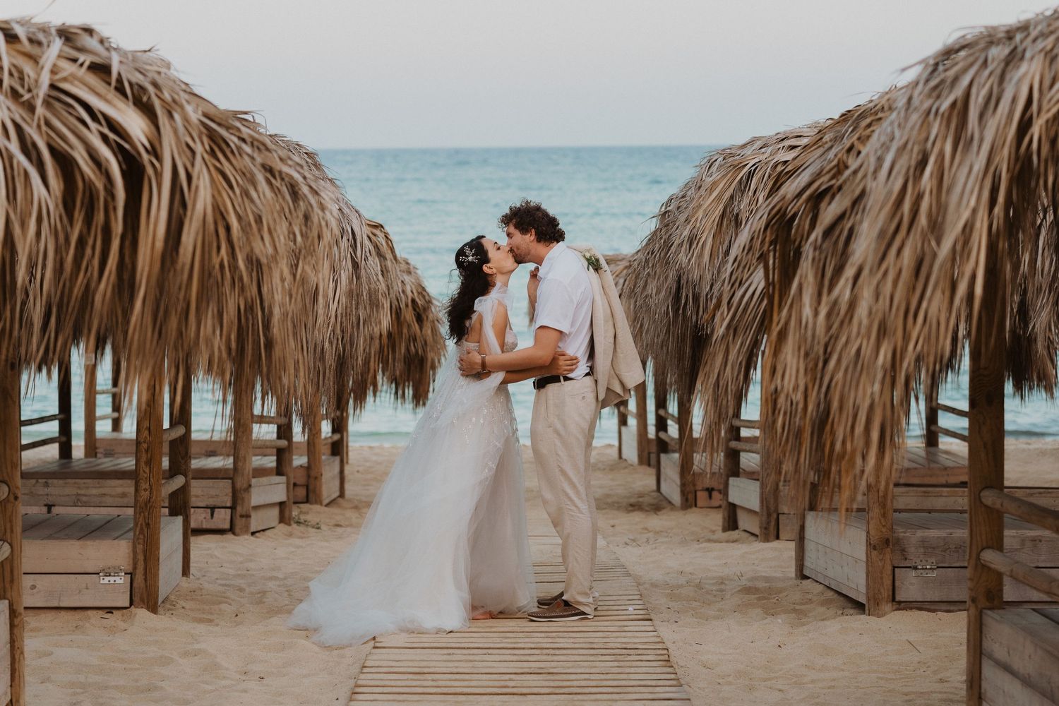 Romantic beach wedding scene between rows of thatched umbrellas.