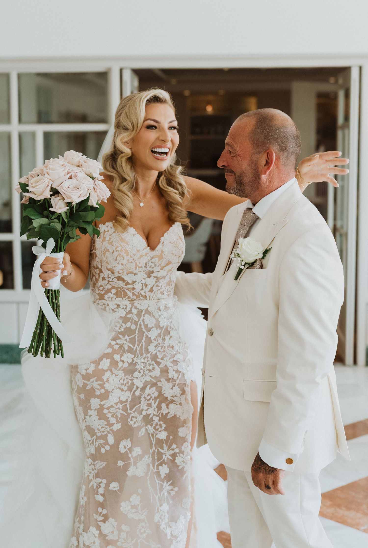 A romantic first look moment between a bride in a sheer floral gown and groom in white suit during their wedding day.