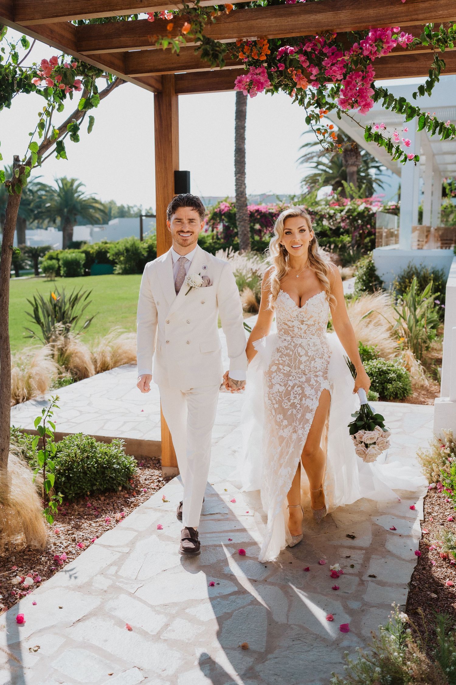 Wedding couple dances under a covered patio with pink bougainvillea flowers and scattered rose petals on the ground.