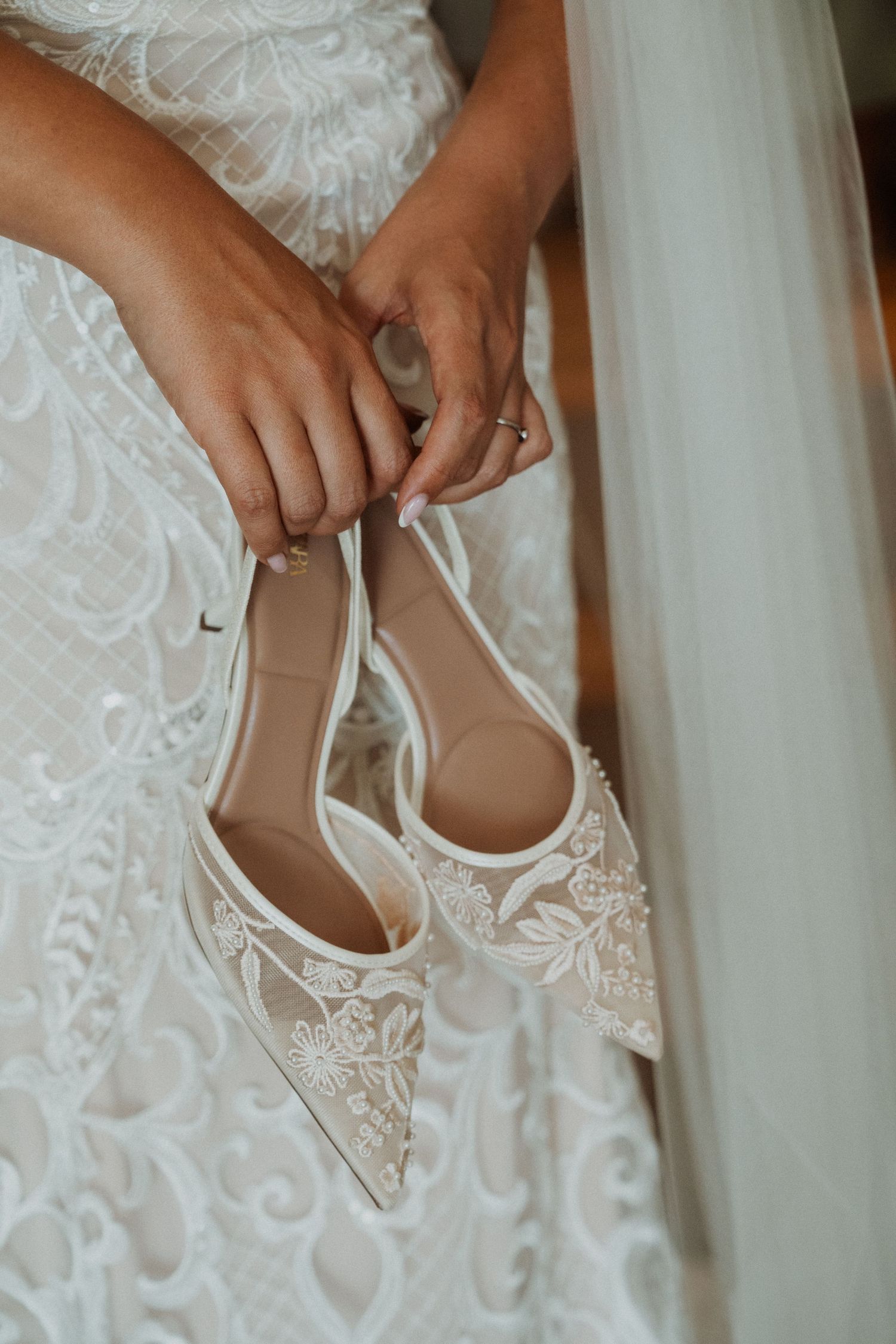 Close-up of delicate white lace wedding shoes being put on.