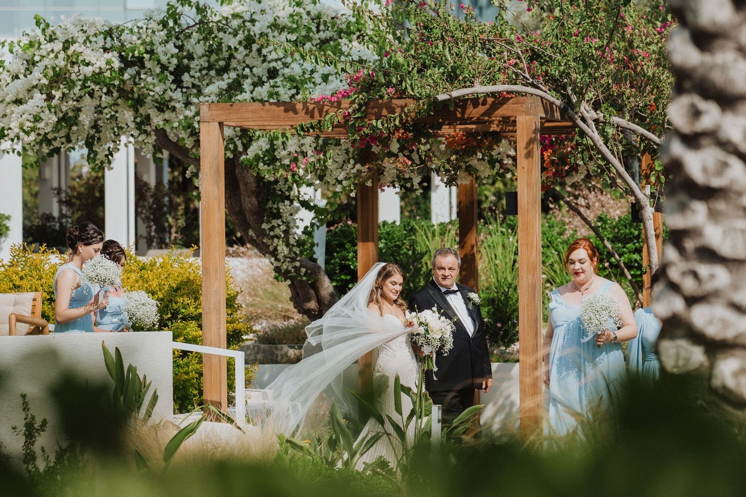 Bride and groom walking through a garden pergola decorated with flowers at their wedding.