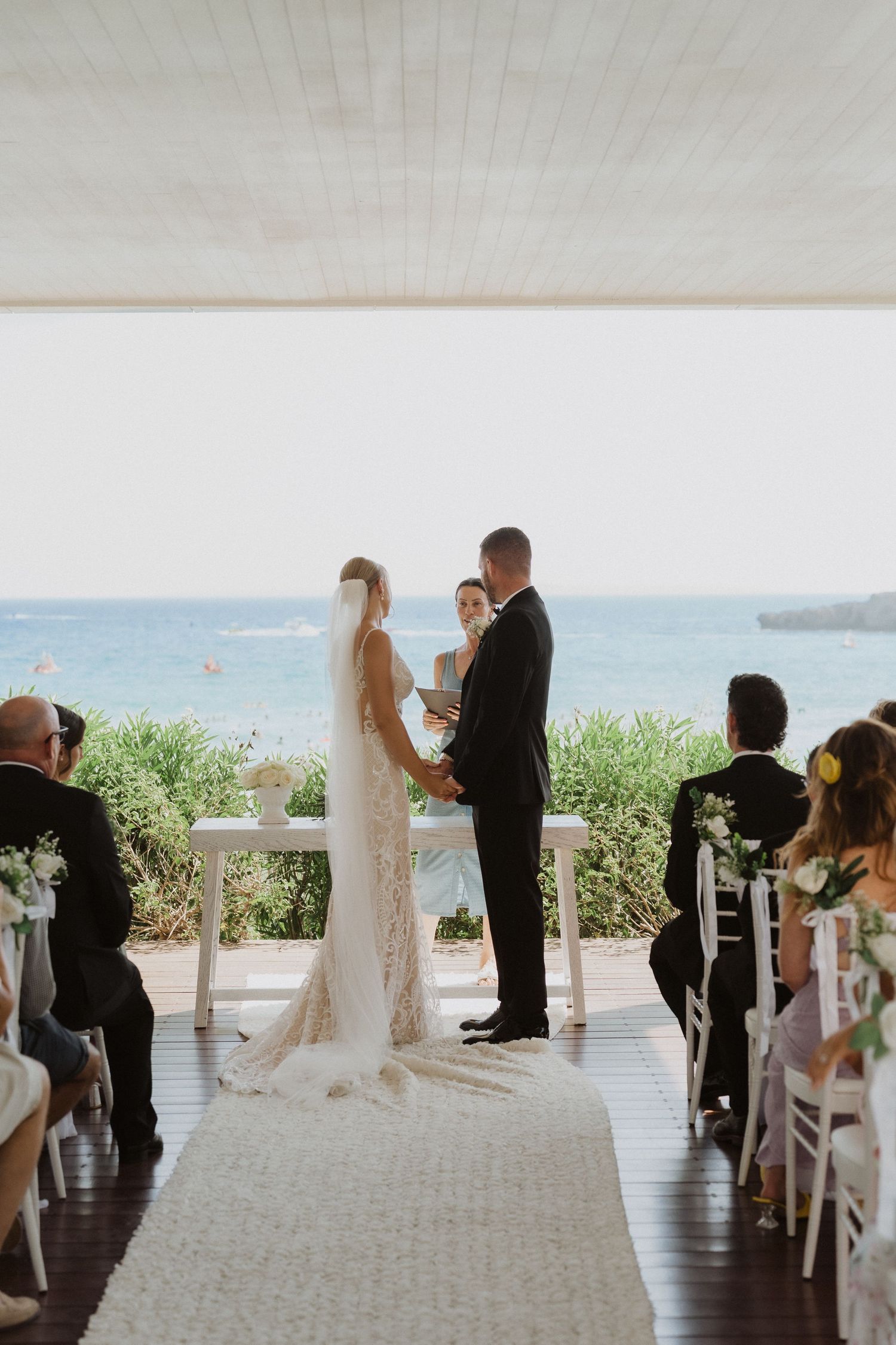 Oceanfront wedding ceremony with couple exchanging vows on covered terrace.