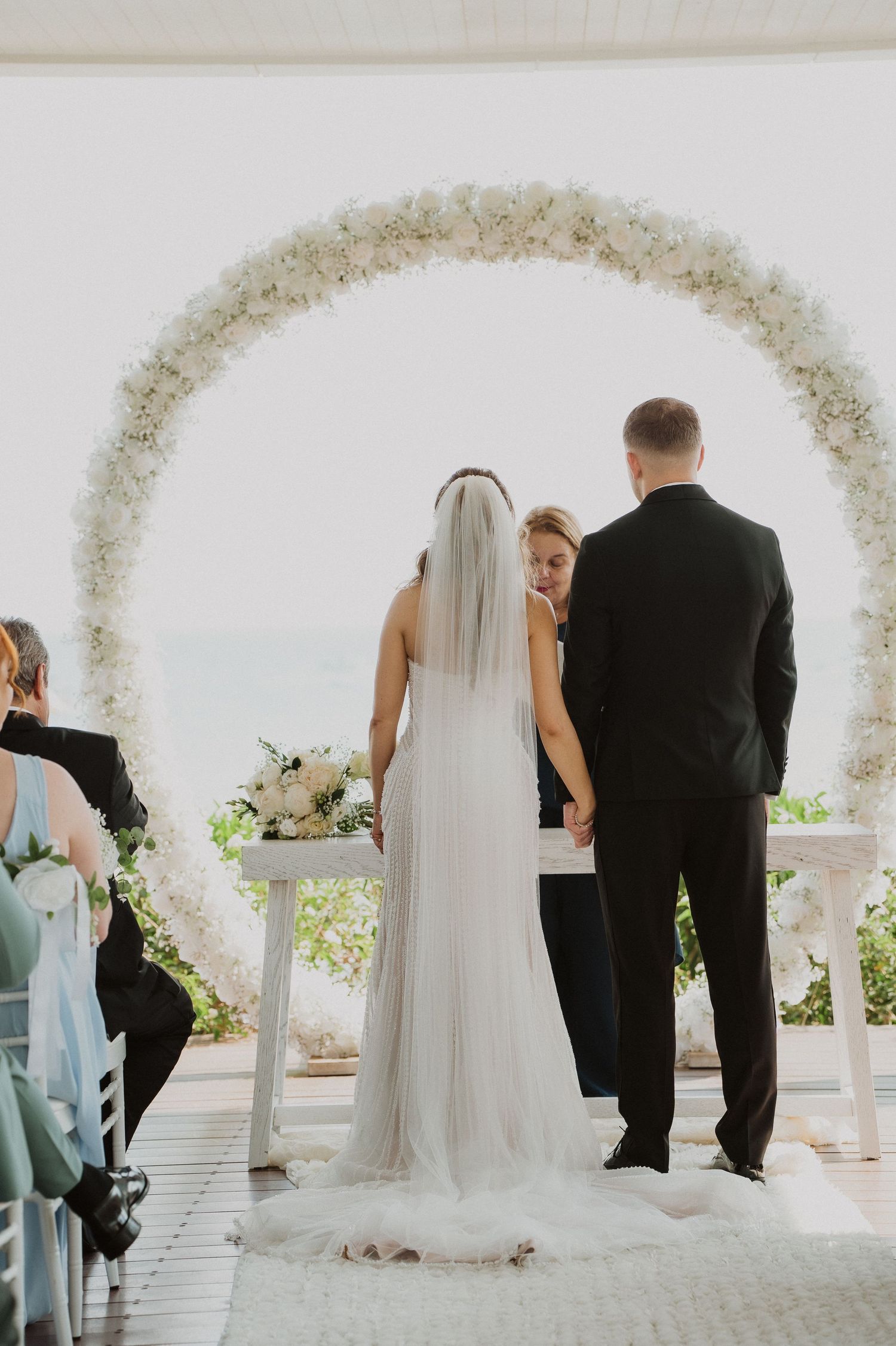 Bride and groom exchanging vows beneath stunning circular white floral arch at outdoor ceremony.