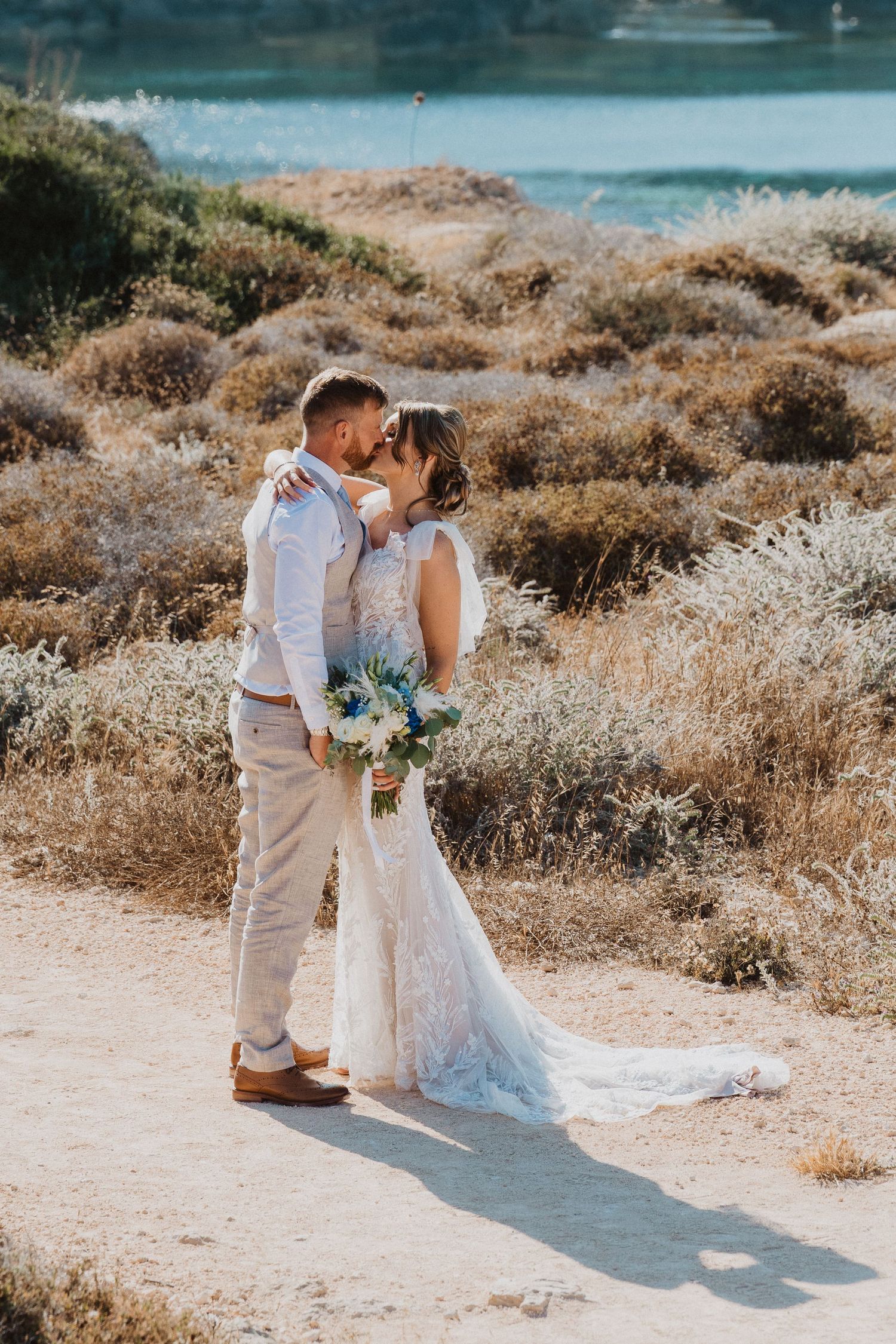 Newlyweds share an intimate moment on a coastal path with ocean views.