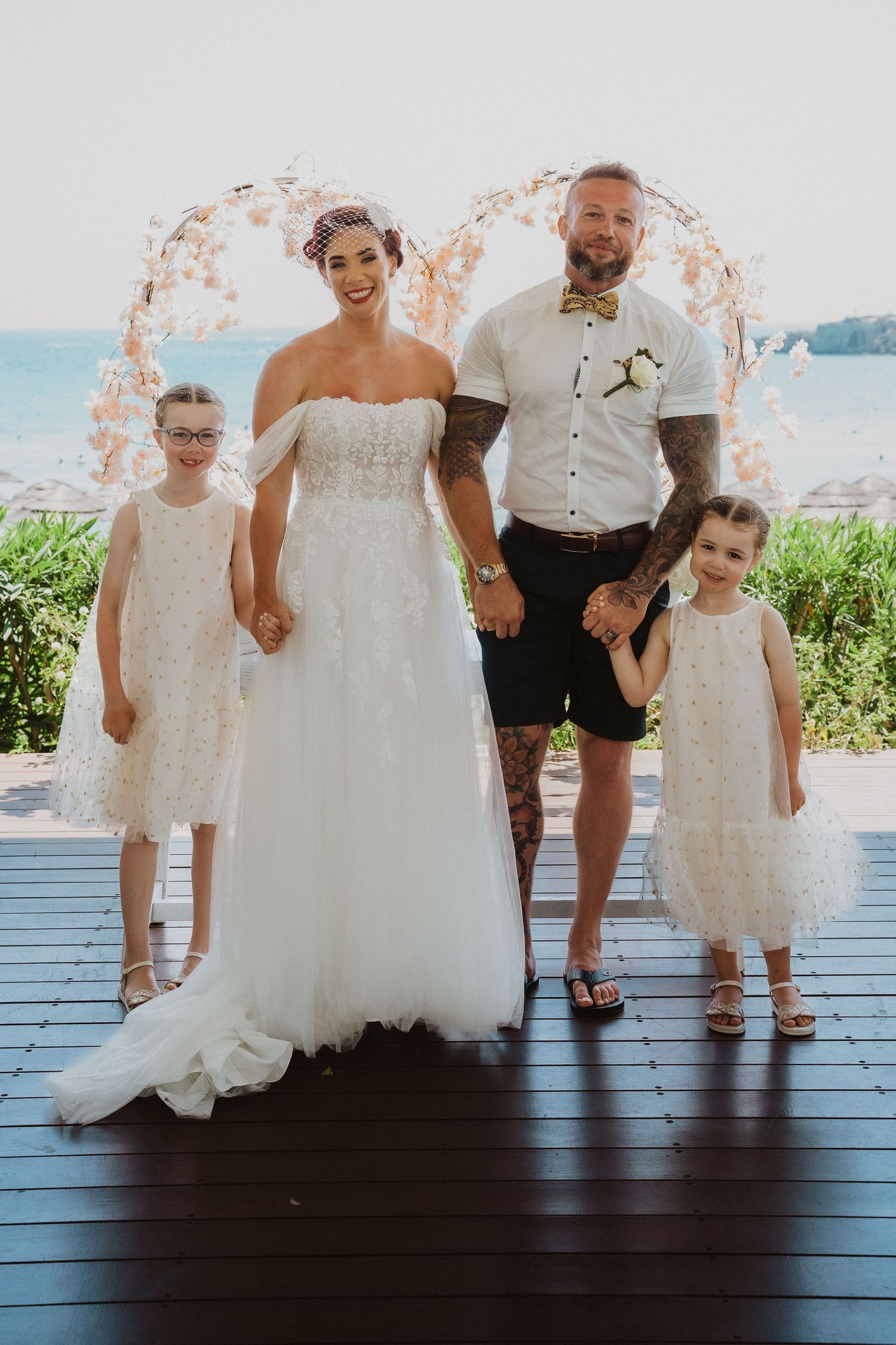 Family portrait at a beach wedding with two small children in matching white dresses.
