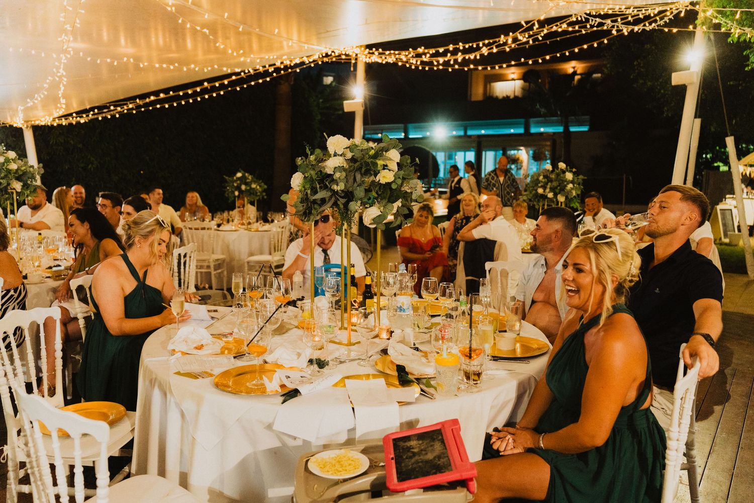 Wedding reception dinner scene with decorated tables and warm ambient lighting under tent.