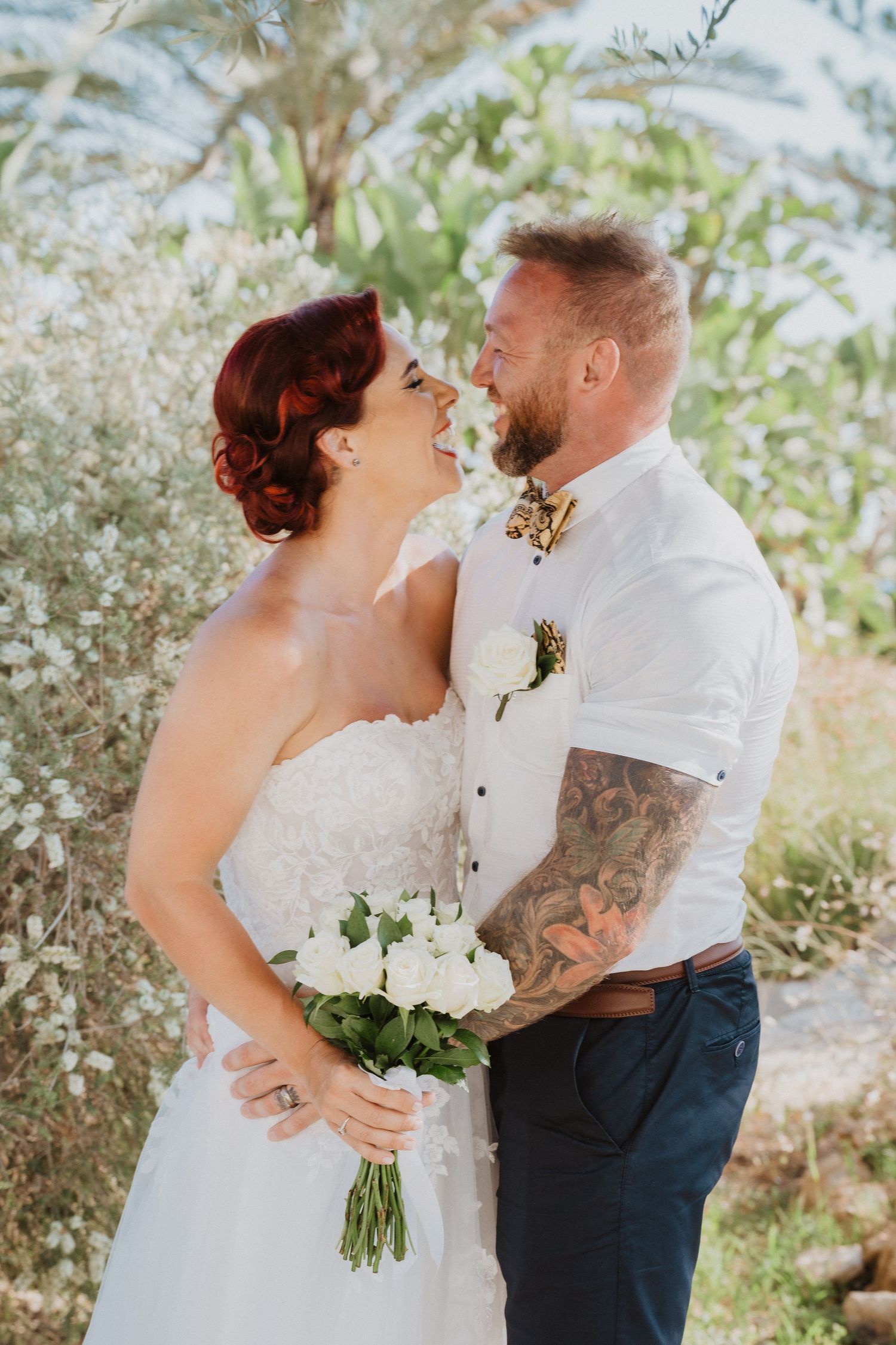 Happy couple shares joyful moment while holding white floral bouquet outdoors.