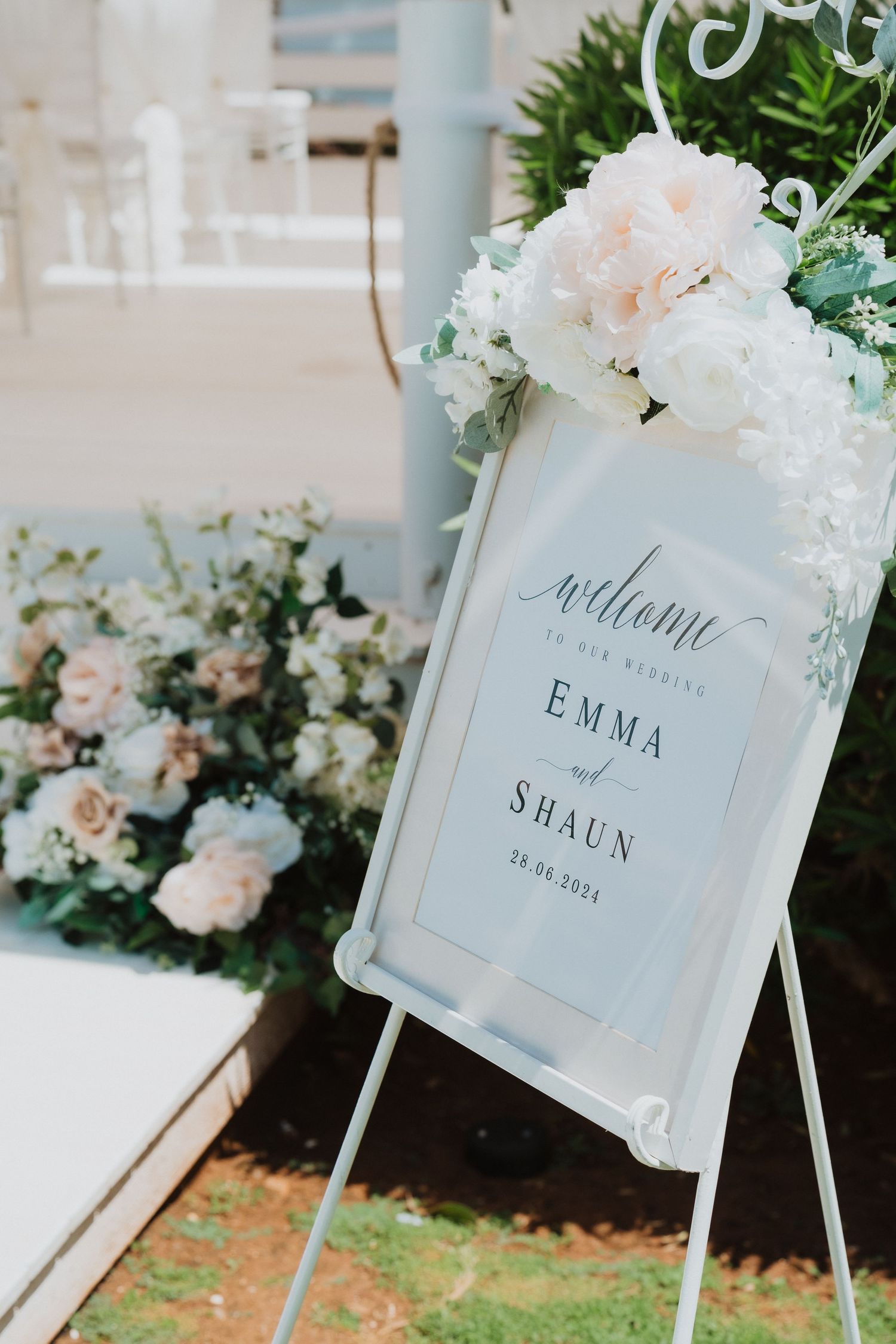 Elegant wedding welcome sign with white floral decorations and calligraphy text.