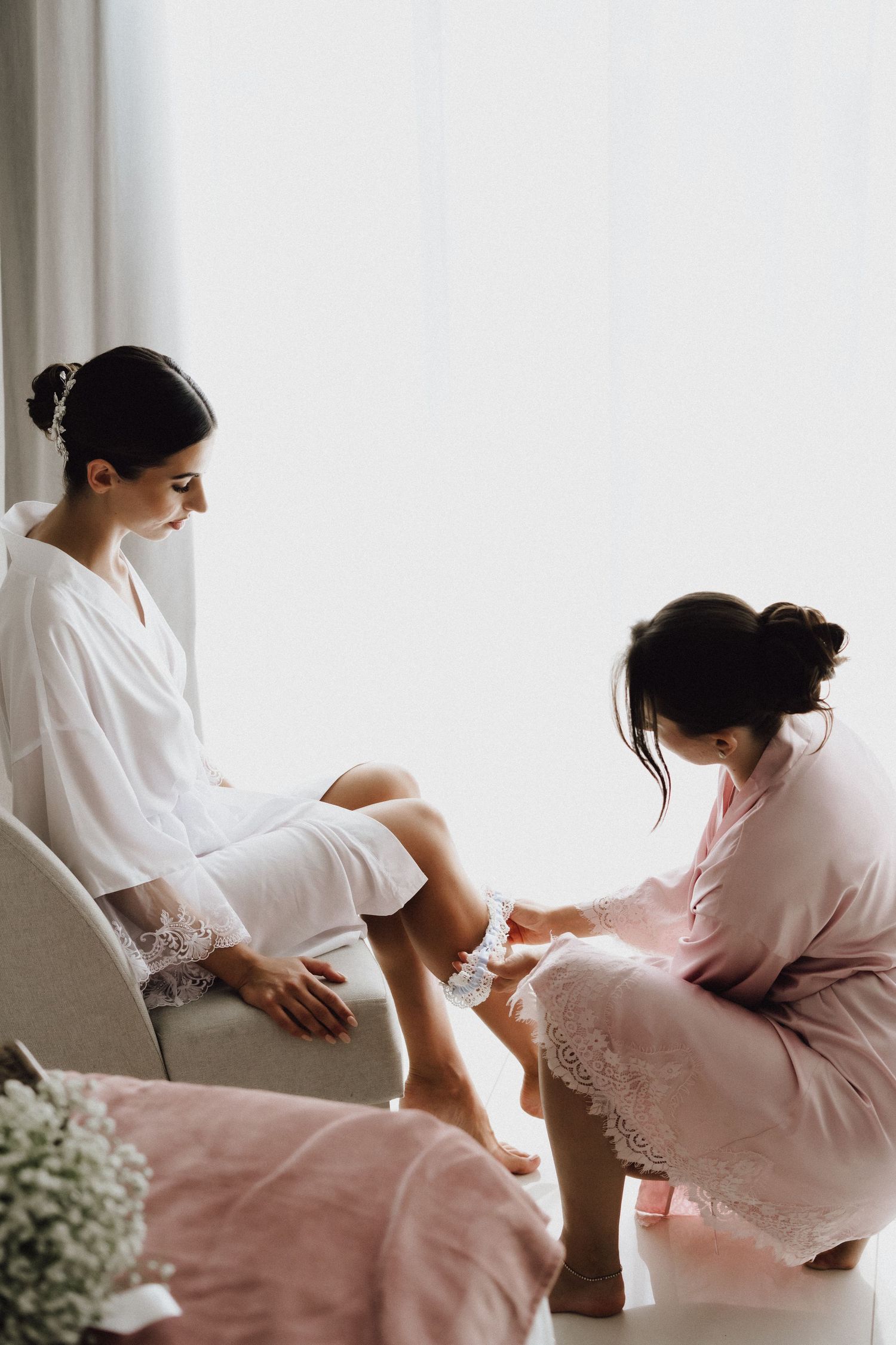 Person in pink robe attends to someone seated in white robe during preparation session.
