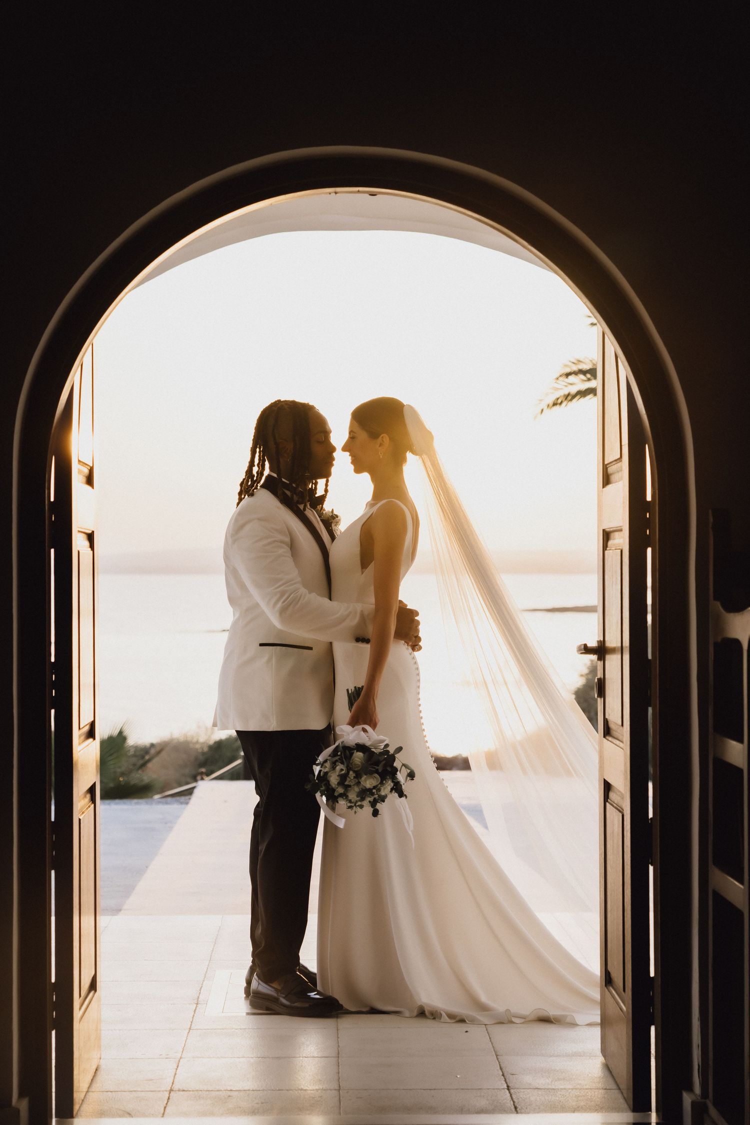 A sunset wedding portrait through an arched doorway overlooking the ocean.