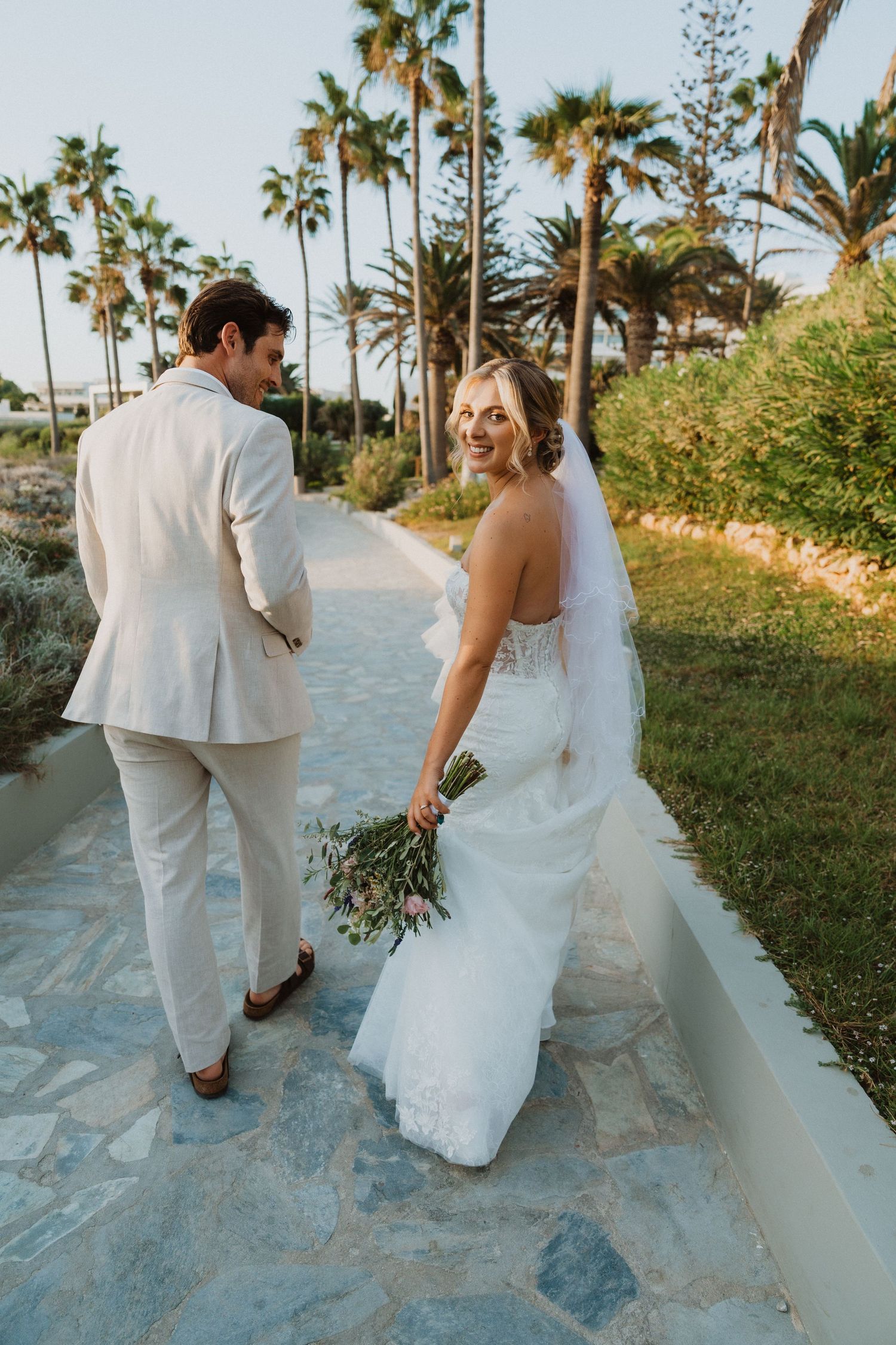 A bride and groom walk along a tropical palm-lined pathway during their destination wedding.