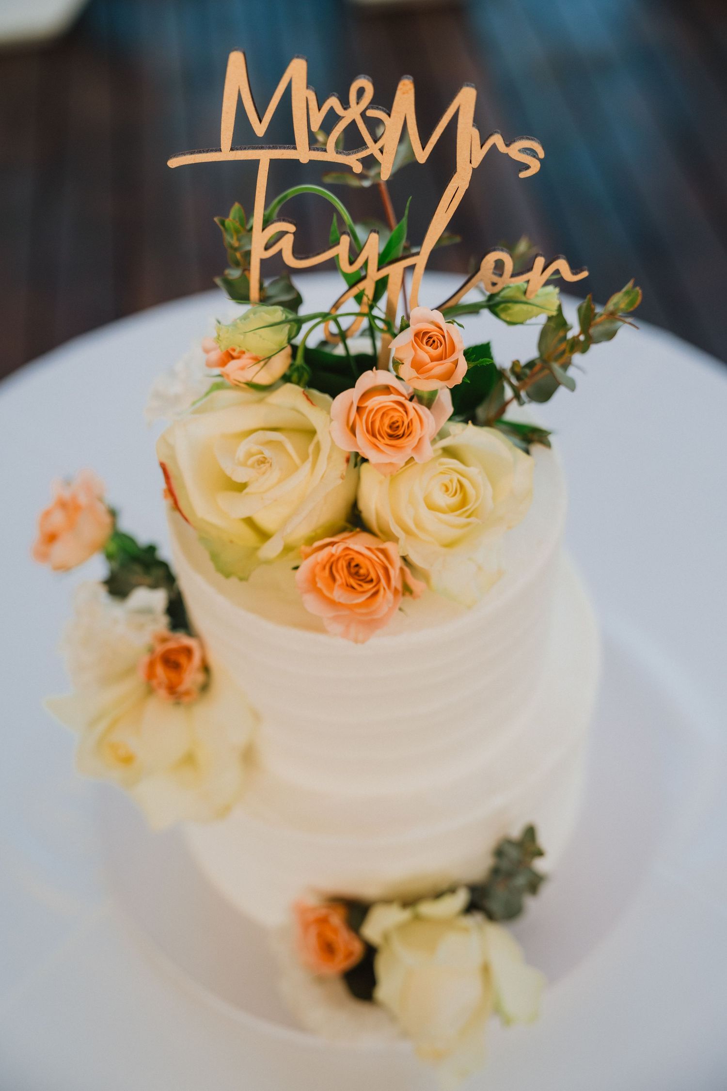 White wedding cake decorated with peach and cream roses and gold Mr & Mrs cake topper.