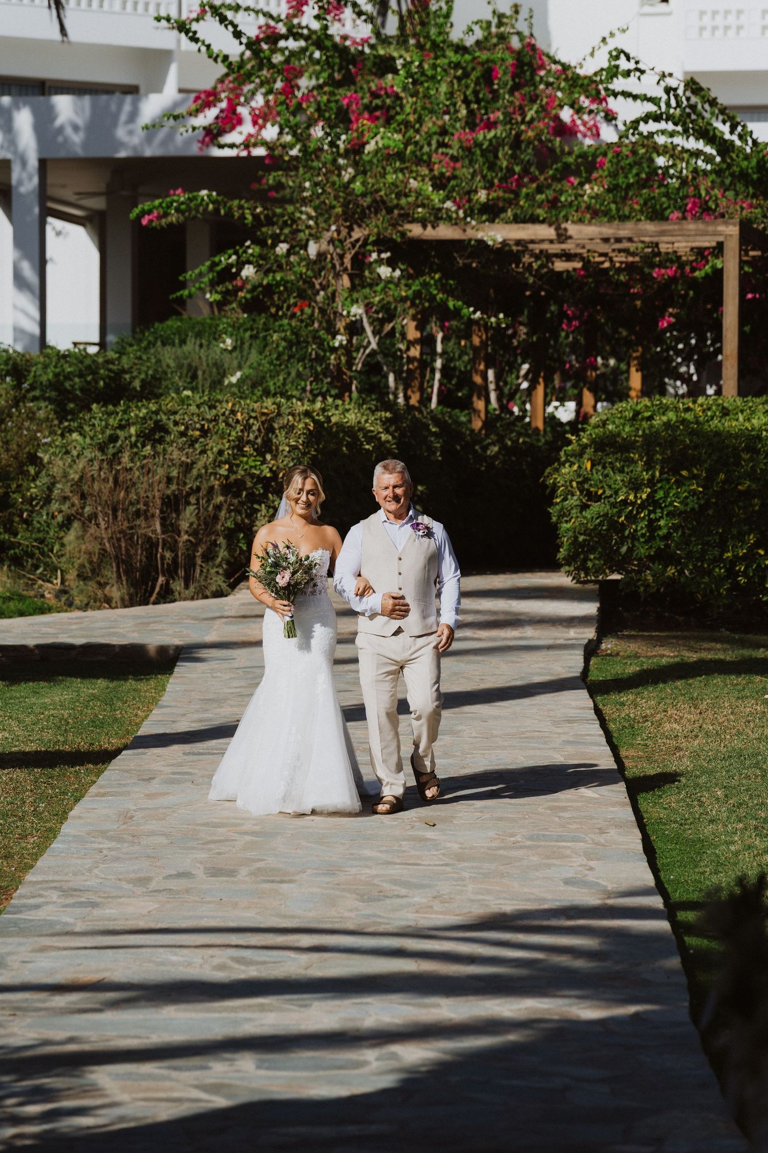 Wedding couple walks along stone pathway surrounded by tropical gardens.