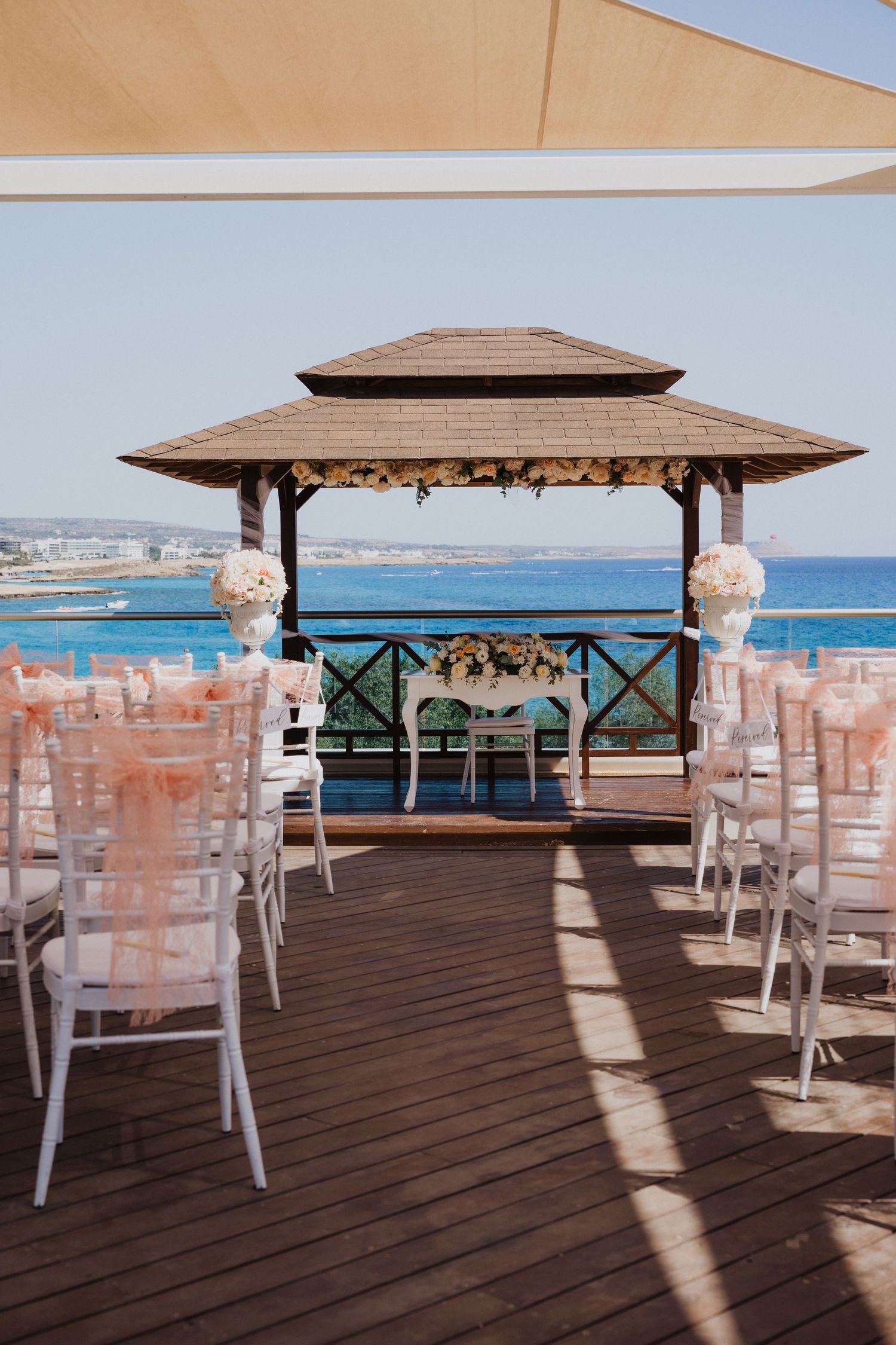 Wooden deck wedding venue with covered gazebos and white chairs arranged for a seaside ceremony.