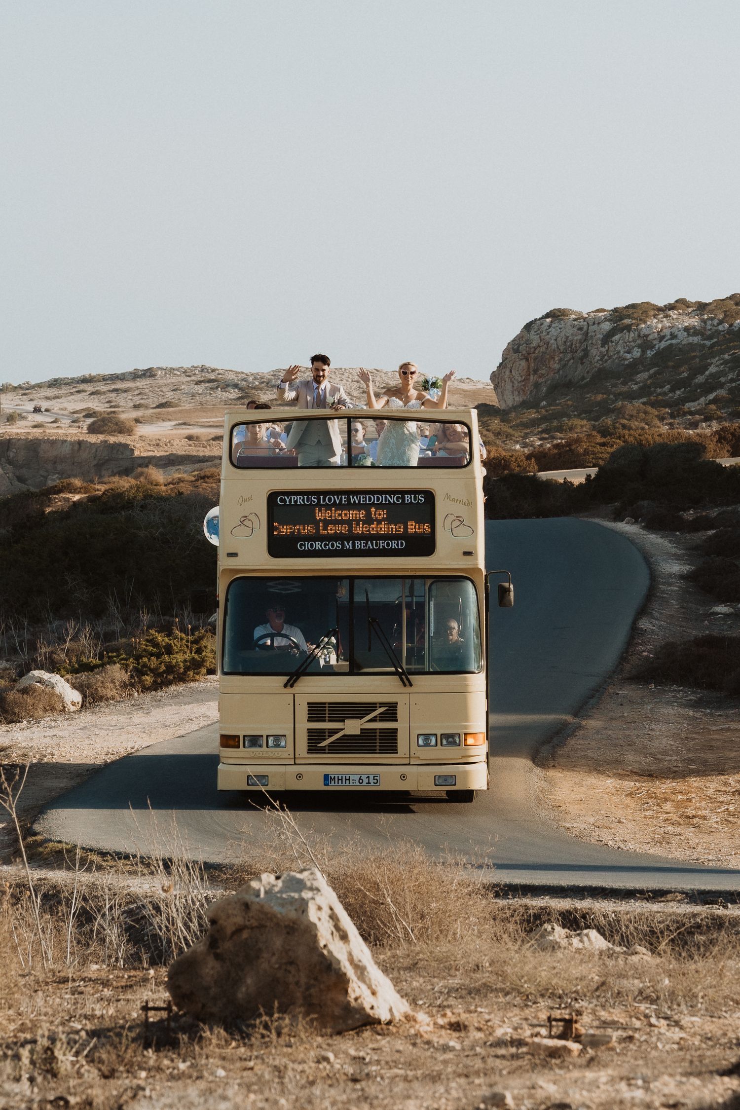 A vintage-style cream colored tour bus parked on a scenic coastal road in Cyprus.