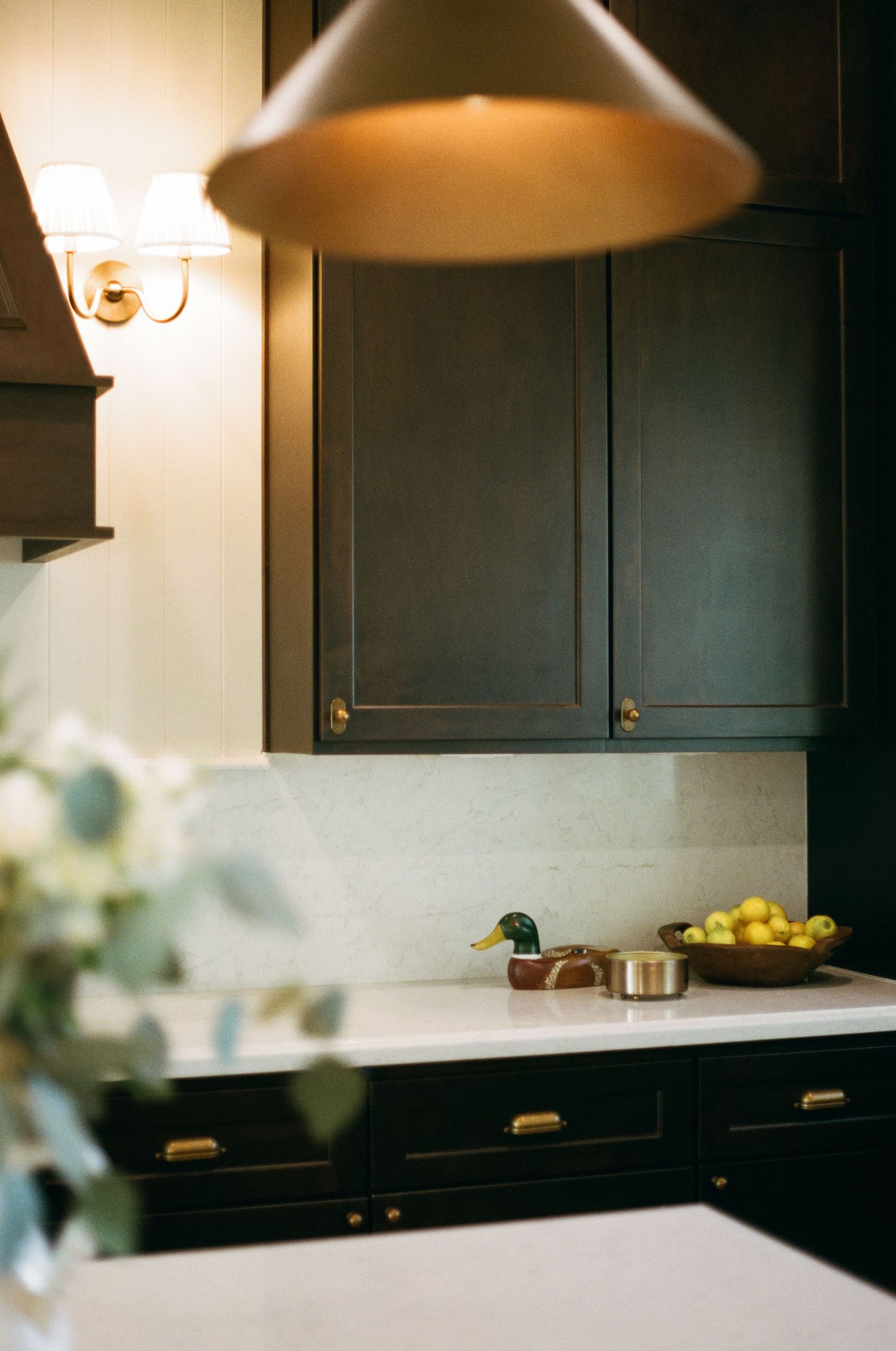 Dark green kitchen cabinets with brass hardware, white marble backsplash, and warm pendant lighting.