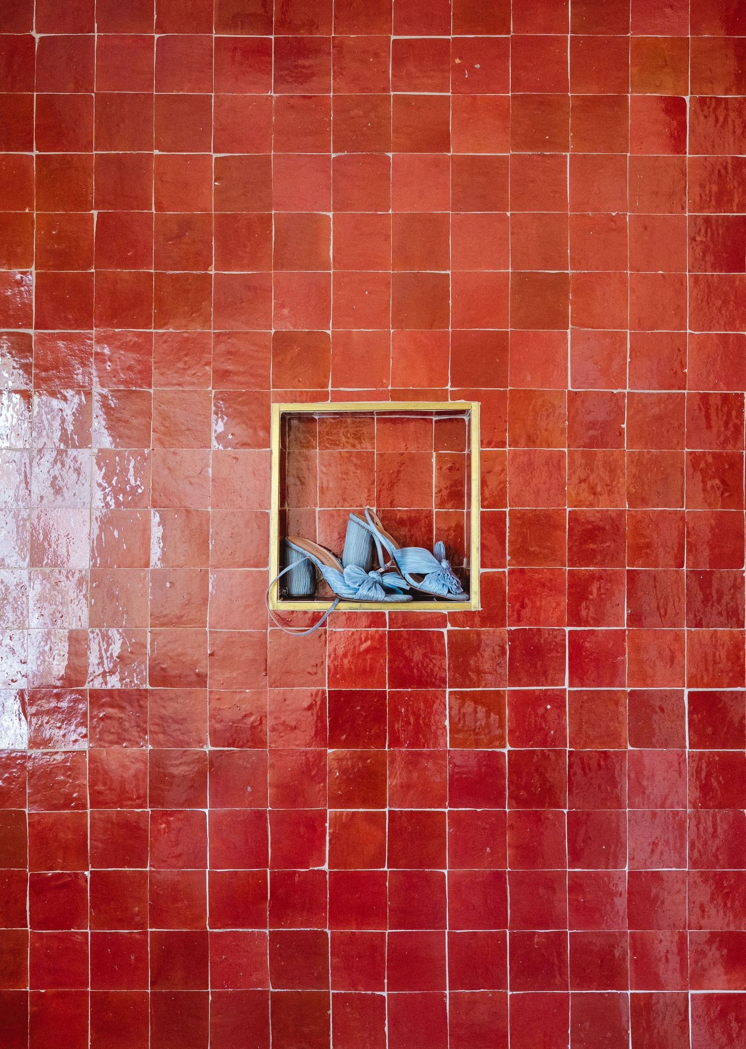 Blue heels displayed in a gold-framed niche set against a vibrant red square-tiled wall.