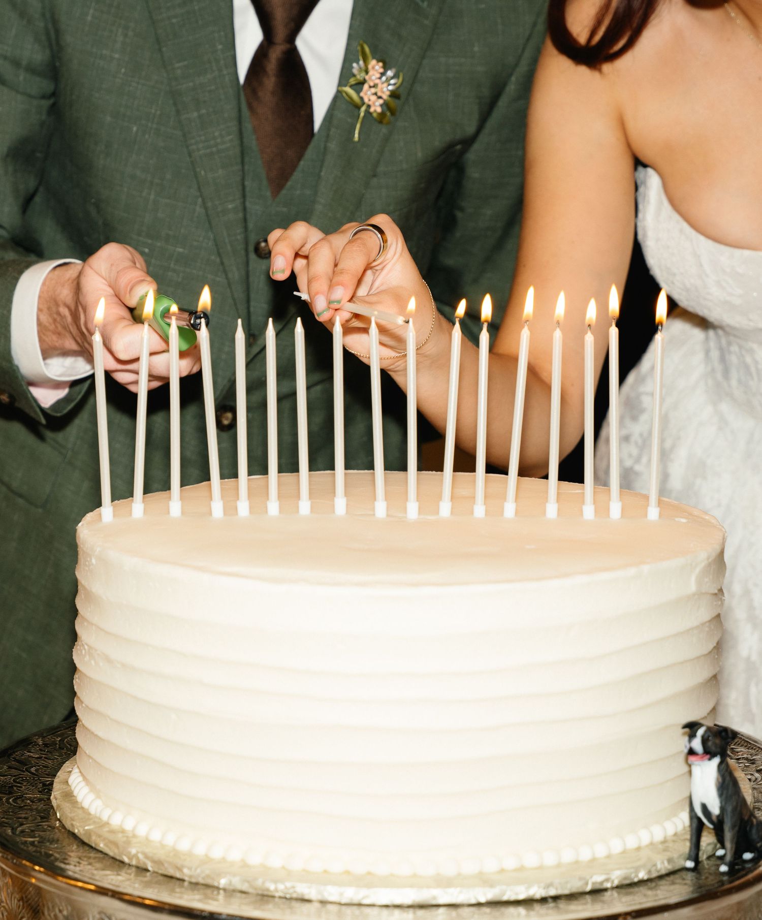 Bride and groom lighting candles on a white single-tier wedding cake with a small dog figurine.