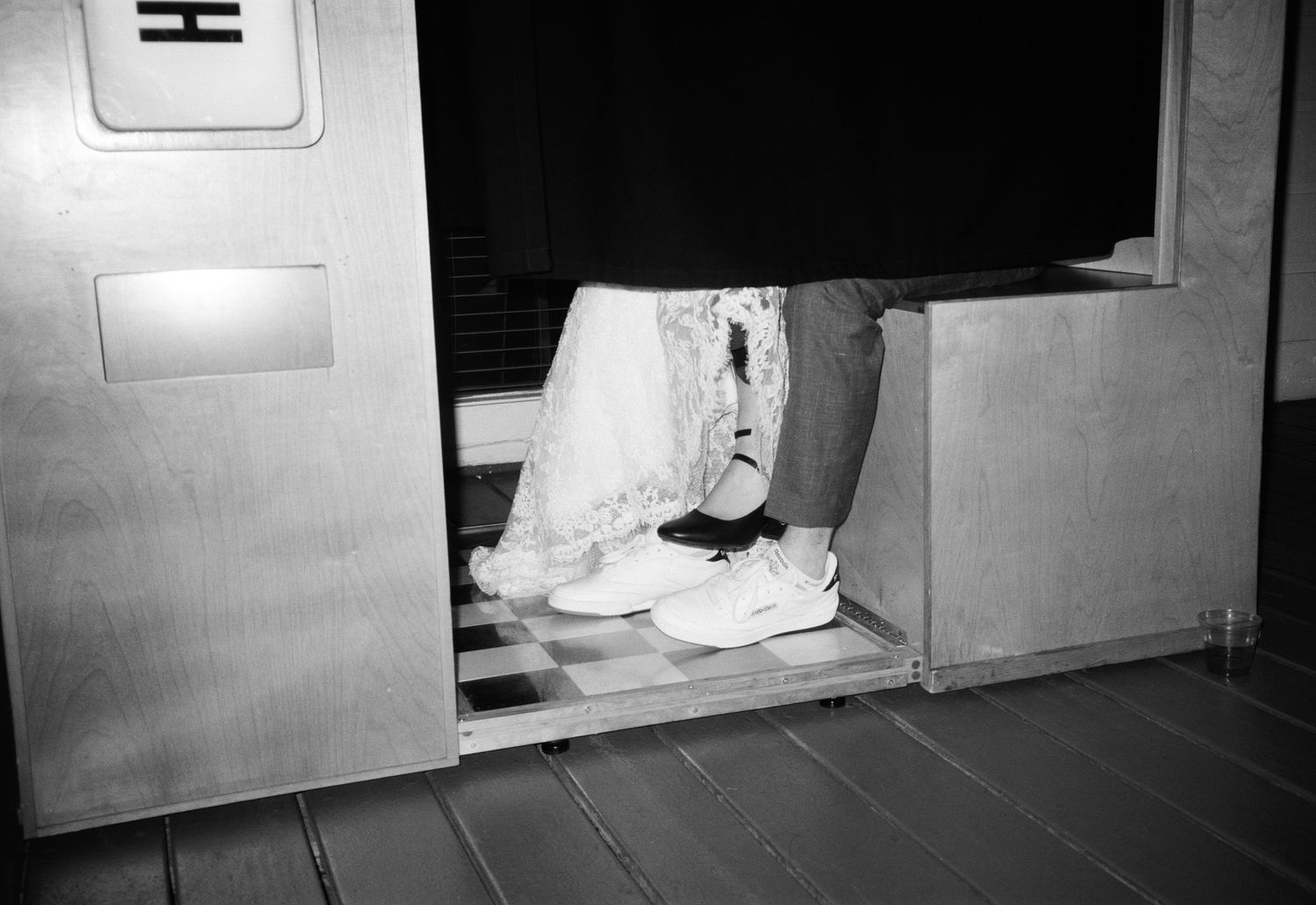 Black and white photo of bride and groom stepping out of vintage photo booth in wedding attire.