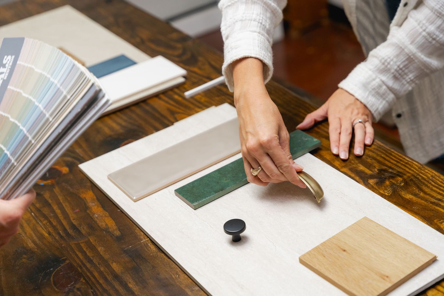 Interior designer presenting material samples, color swatches, and cabinet hardware on a wooden table during a consultation.
