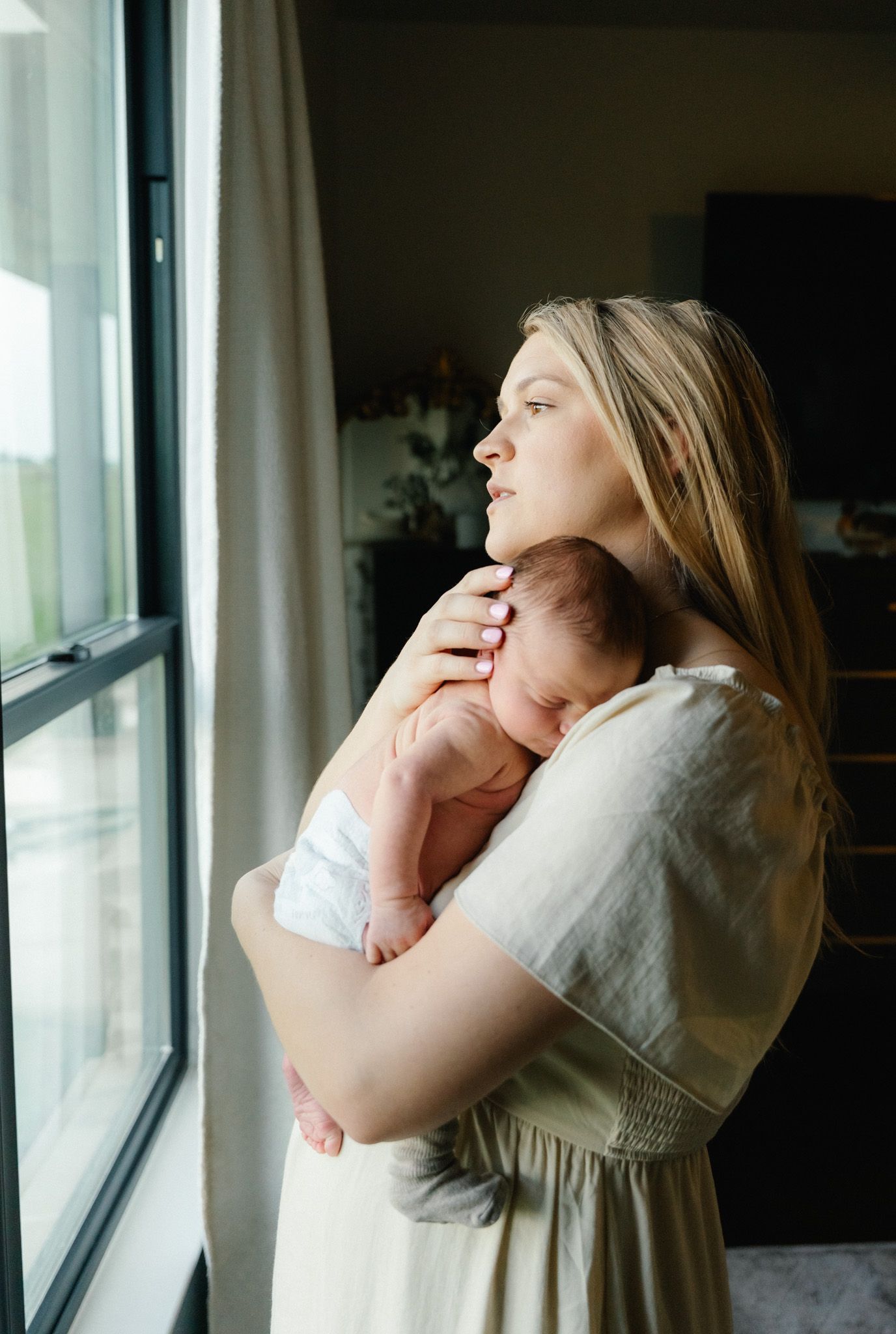 Mother holding her newborn son by a window during an in-home session in East Bernard, Texas.