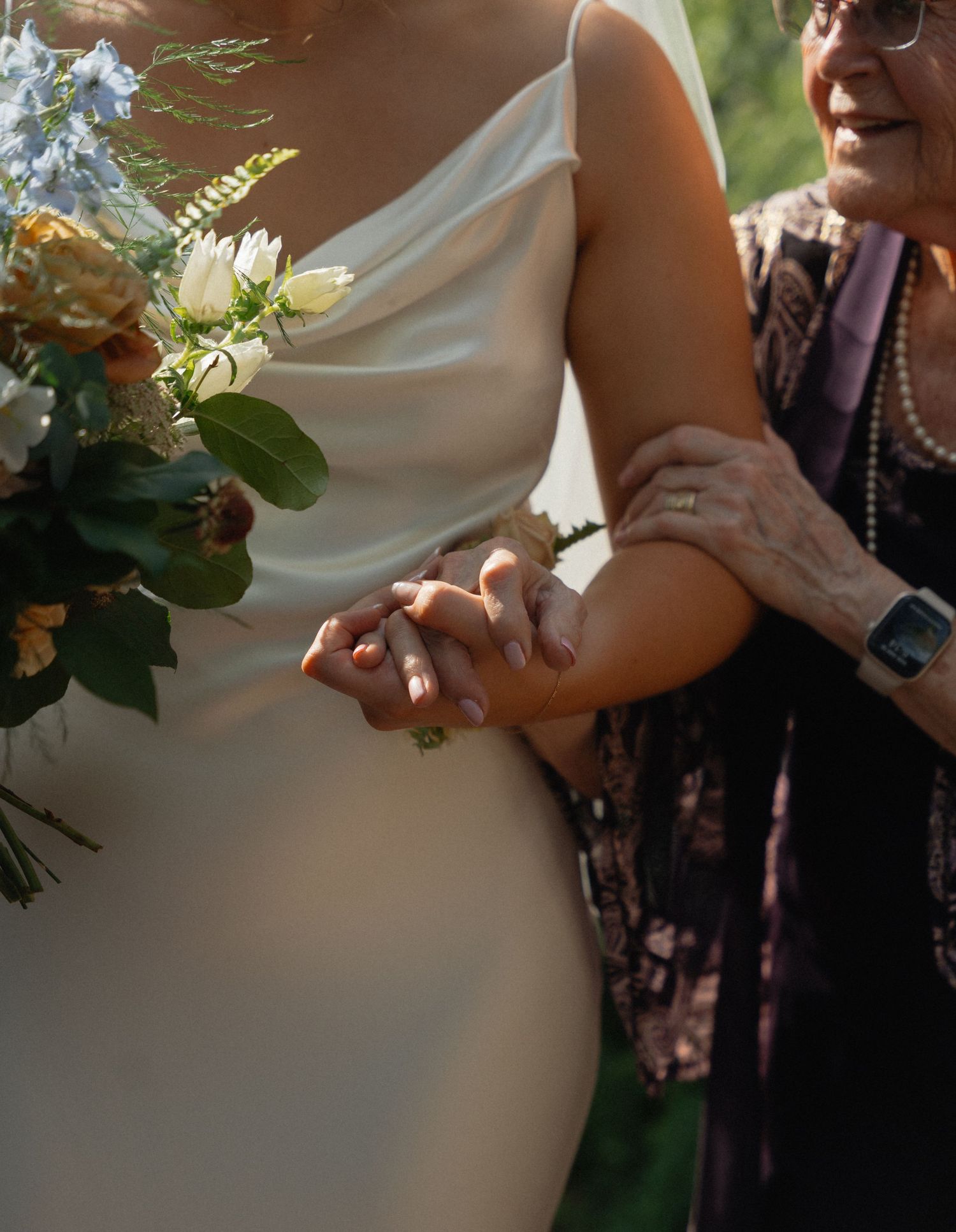 Elderly woman tenderly holding the hand of a bride in a white satin gown holding bouquet.