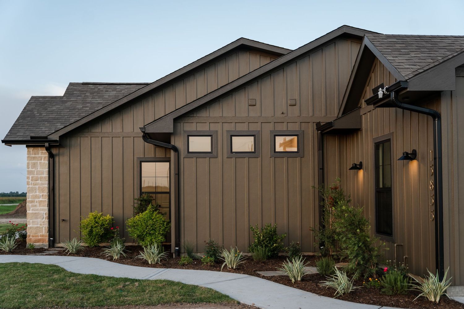 Modern farmhouse exterior with dark brown board-and-batten siding, stone accents, and drought-resistant landscaping.