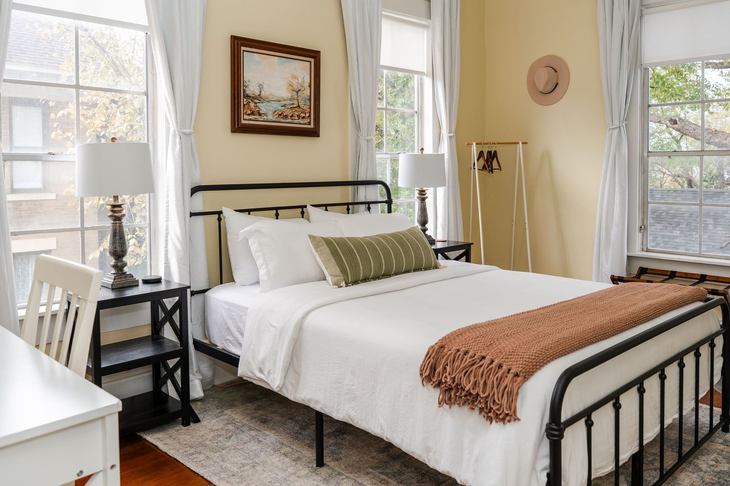 Classic bedroom with black iron bed, white bedding, rust throw blanket, striped pillow, and bright natural light.