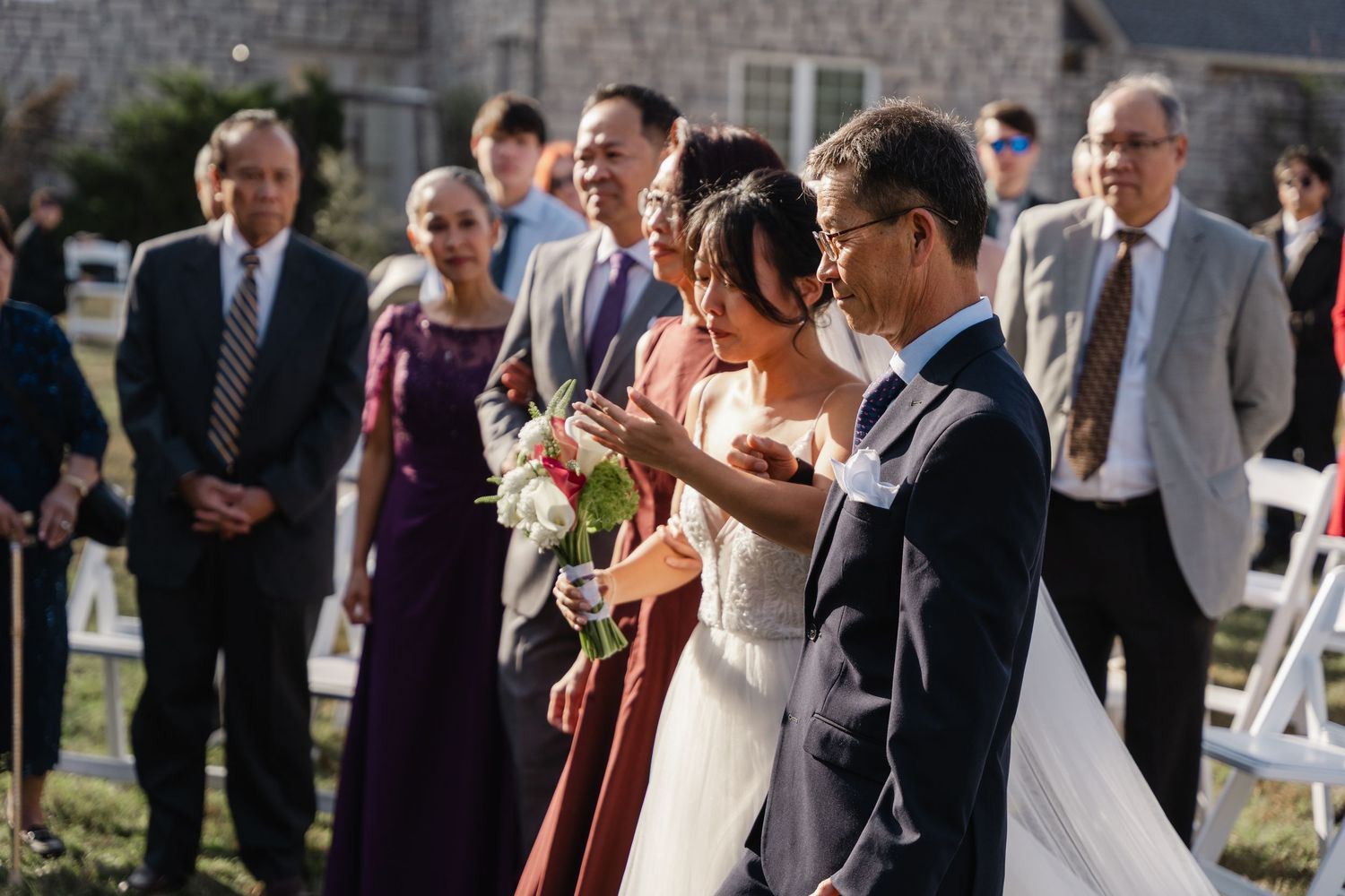 Bride walks down outdoor wedding aisle escorted by father while guests watch the ceremony.