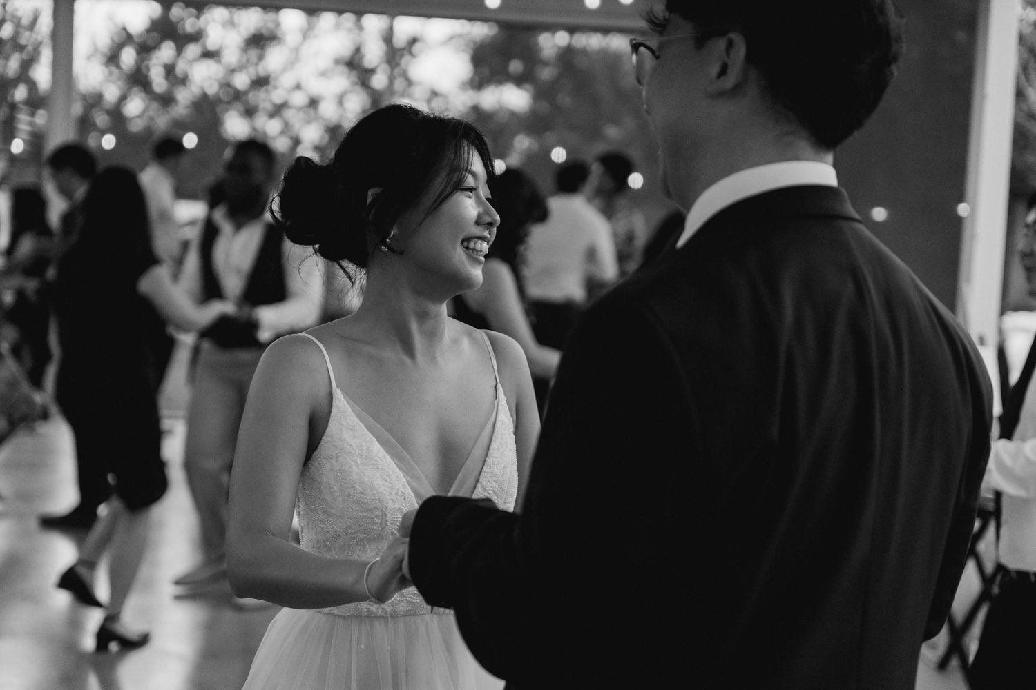 Black and white photo of joyful bride smiling at groom during first dance at wedding reception.