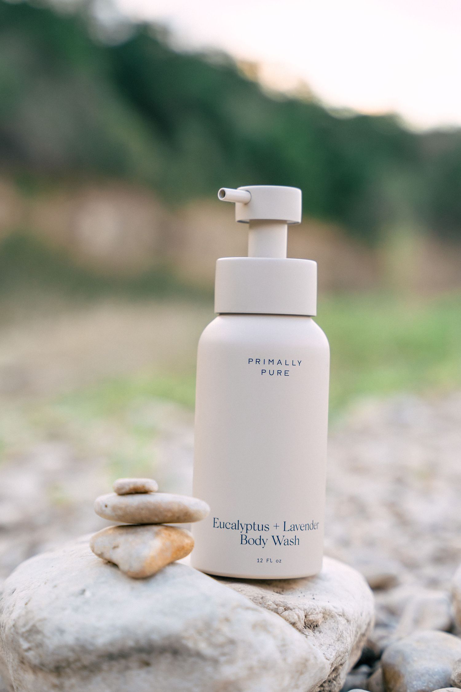 Primally Pure Eucalyptus and Lavender Body Wash pump bottle balanced on stacked stones outdoors.