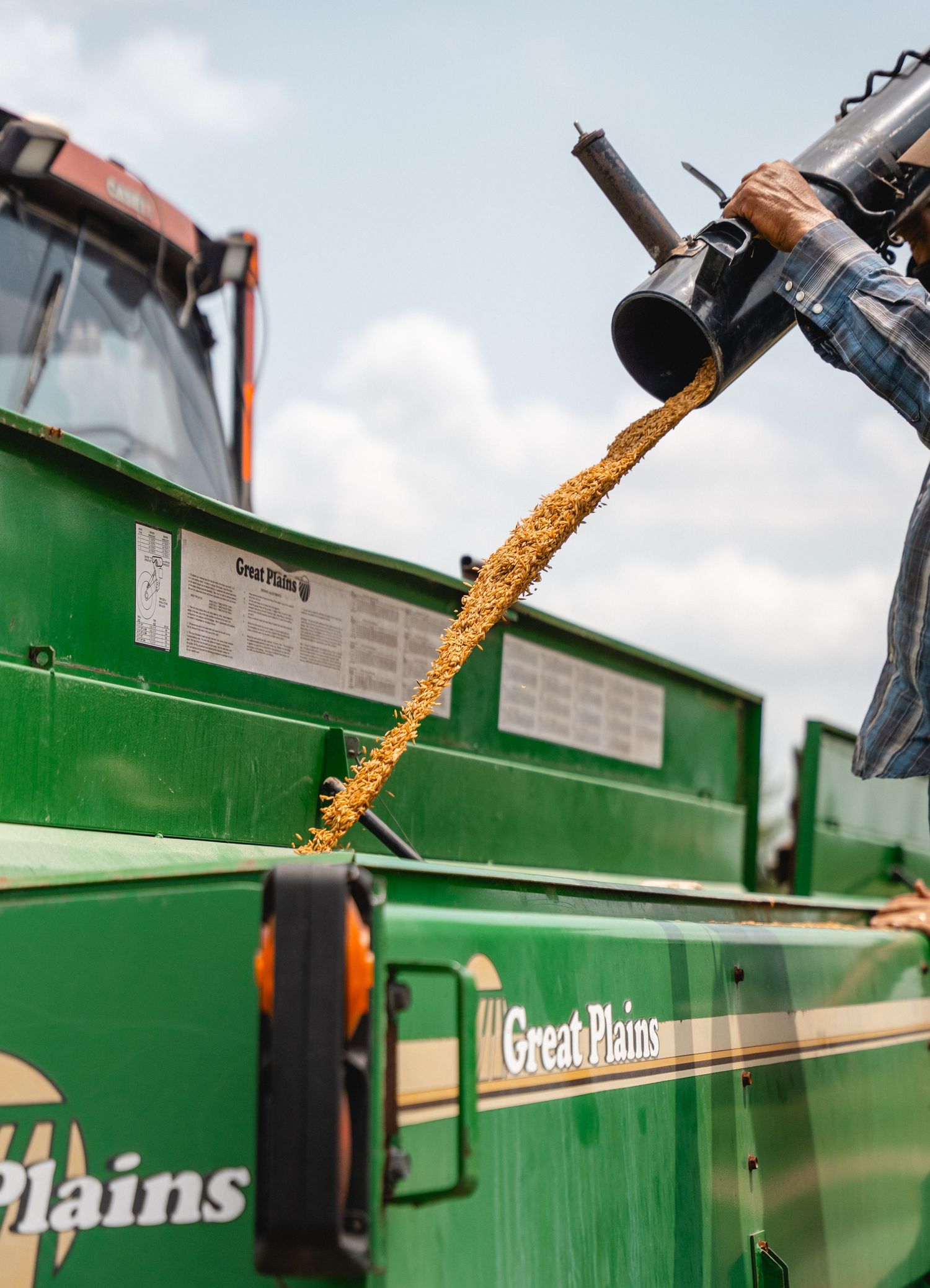 Grain being transferred into a green Great Plains agricultural spreader on a farm.
