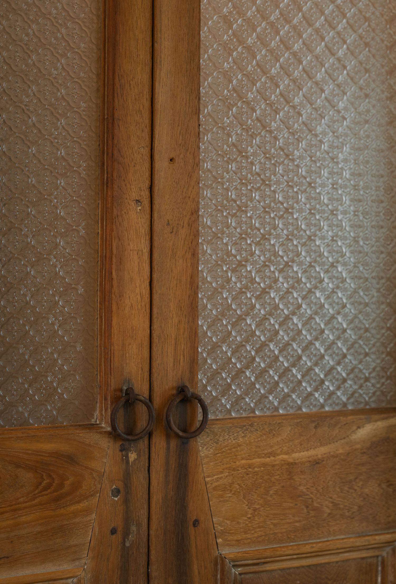 Antique wooden double doors with ornate iron ring handles and textured glass panels set in a classic interior.