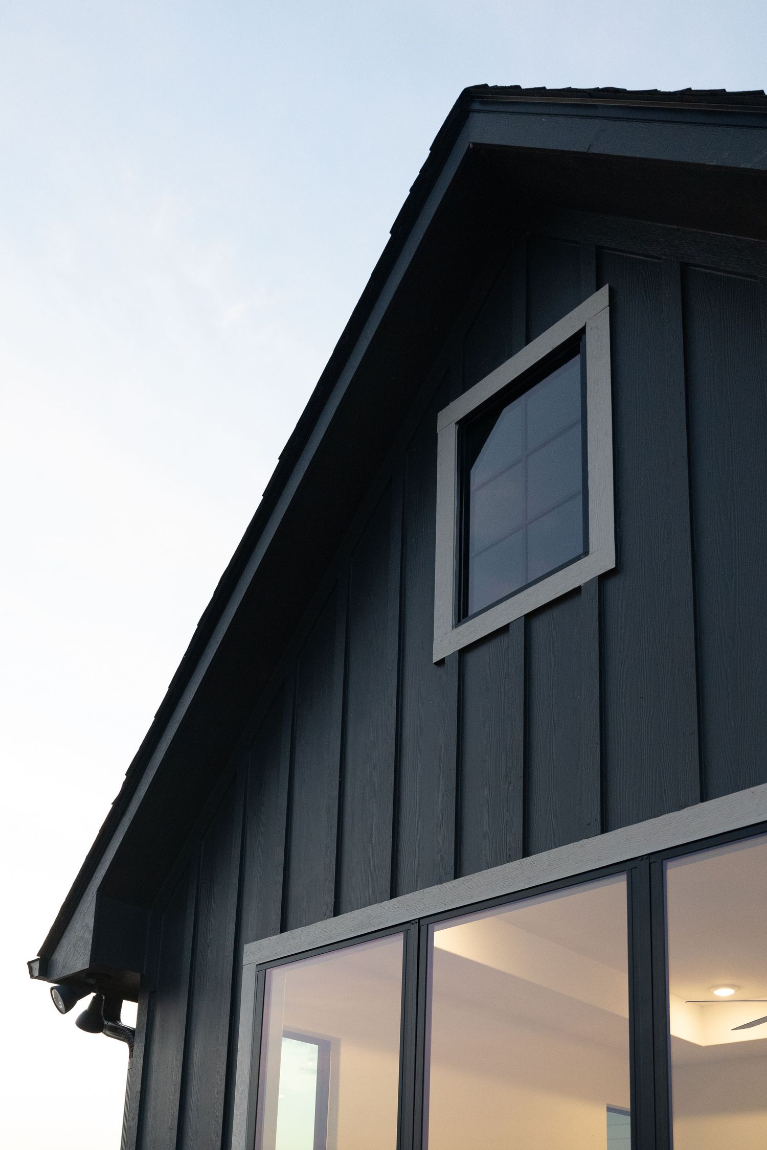 Dark gray board and batten exterior siding with large windows and a diamond accent window on a modern farmhouse gable.