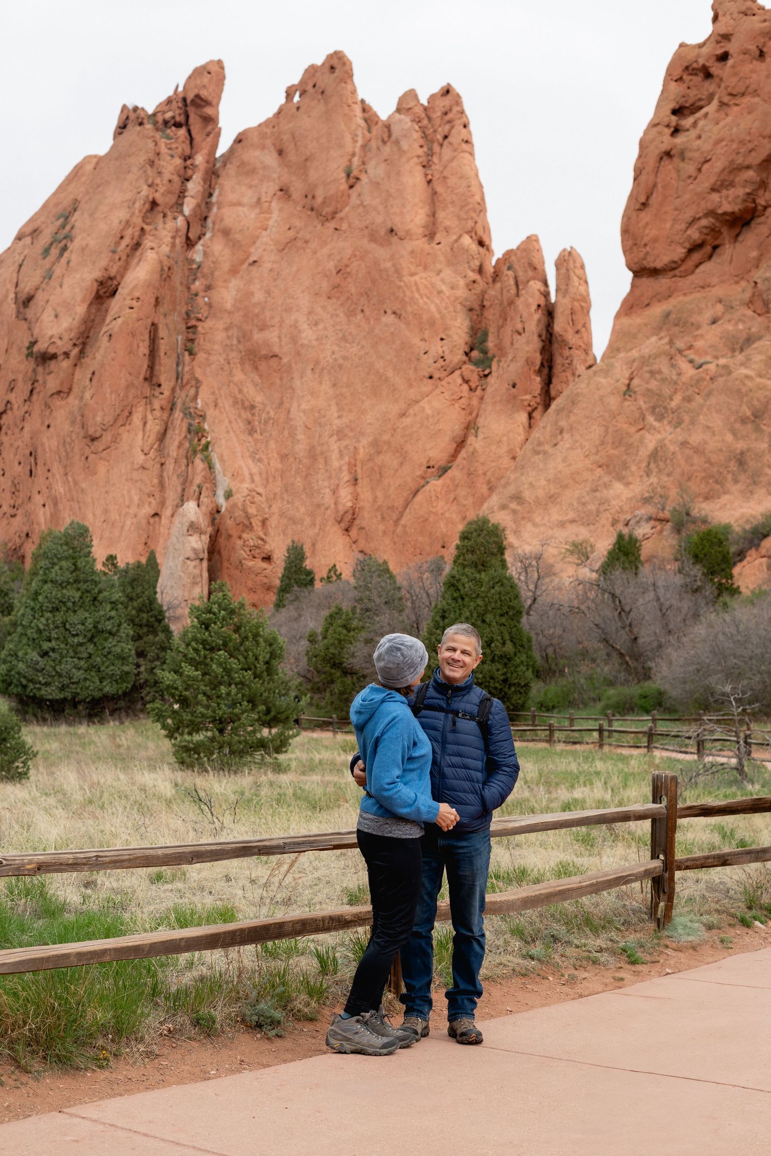 Couple holds hands on paved path with stunning red sandstone spires at Garden of the Gods, Colorado.